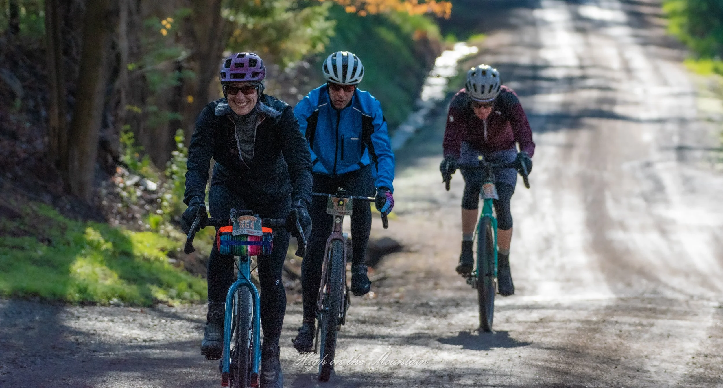 Three women riding bicycles on a shaded trail surrounded by trees.