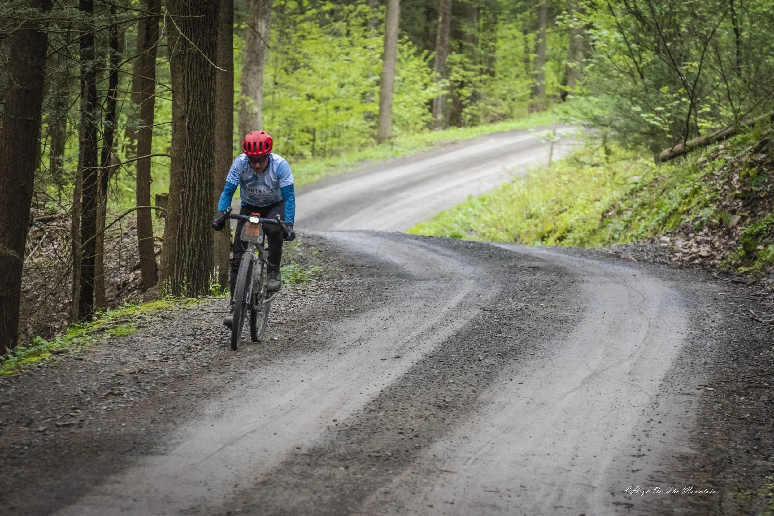 A person wearing a red helmet and blue jacket riding a mountain bike on a dirt trail in a forest with green trees and foliage.