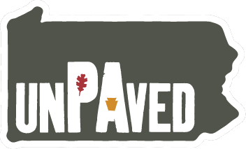 State of Wyoming with the word 'UNPAVED' across it, featuring an oak leaf and a pine cone as part of the text design.