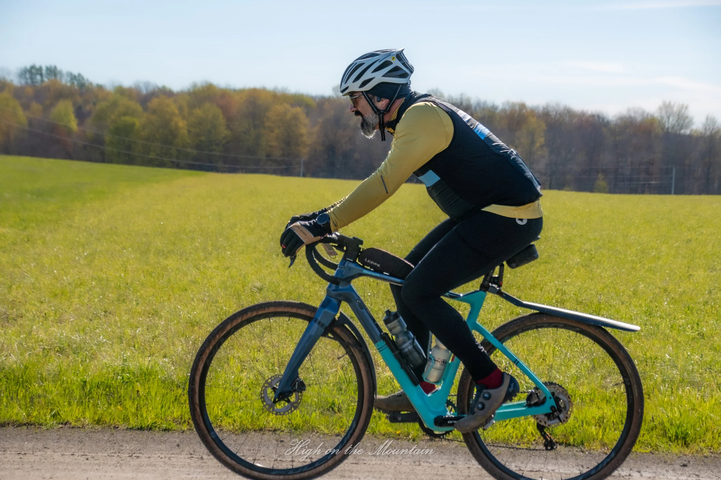 A man wearing a bicycle helmet and sunglasses riding a mountain bike along a path with green grass and trees in the background.