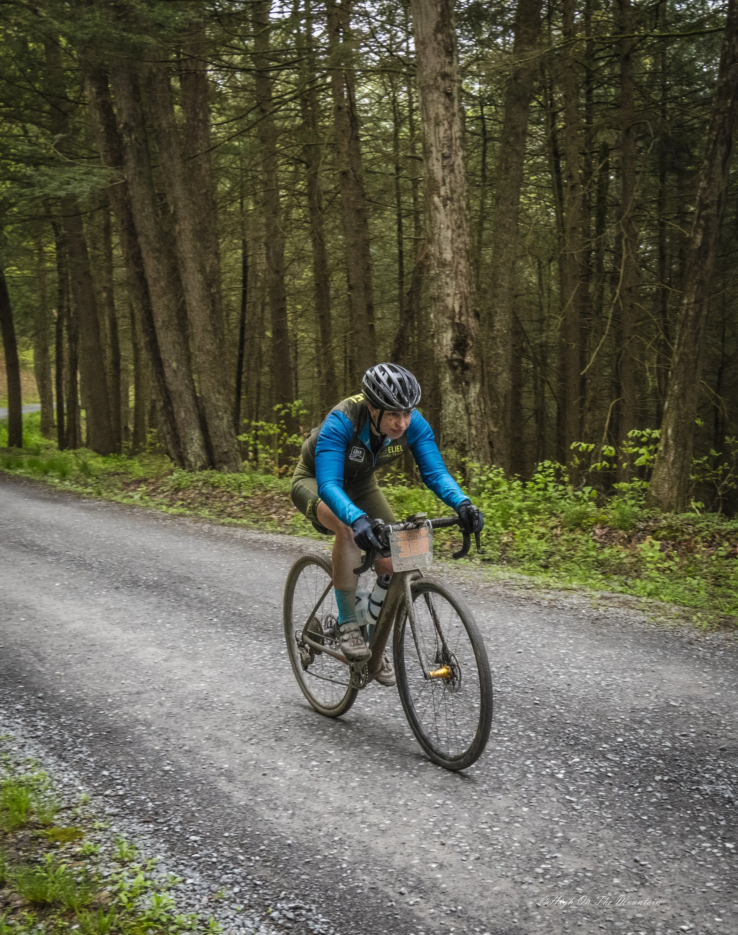 A person riding a mountain bike on a gravel trail in a dense forest with tall trees and green foliage.