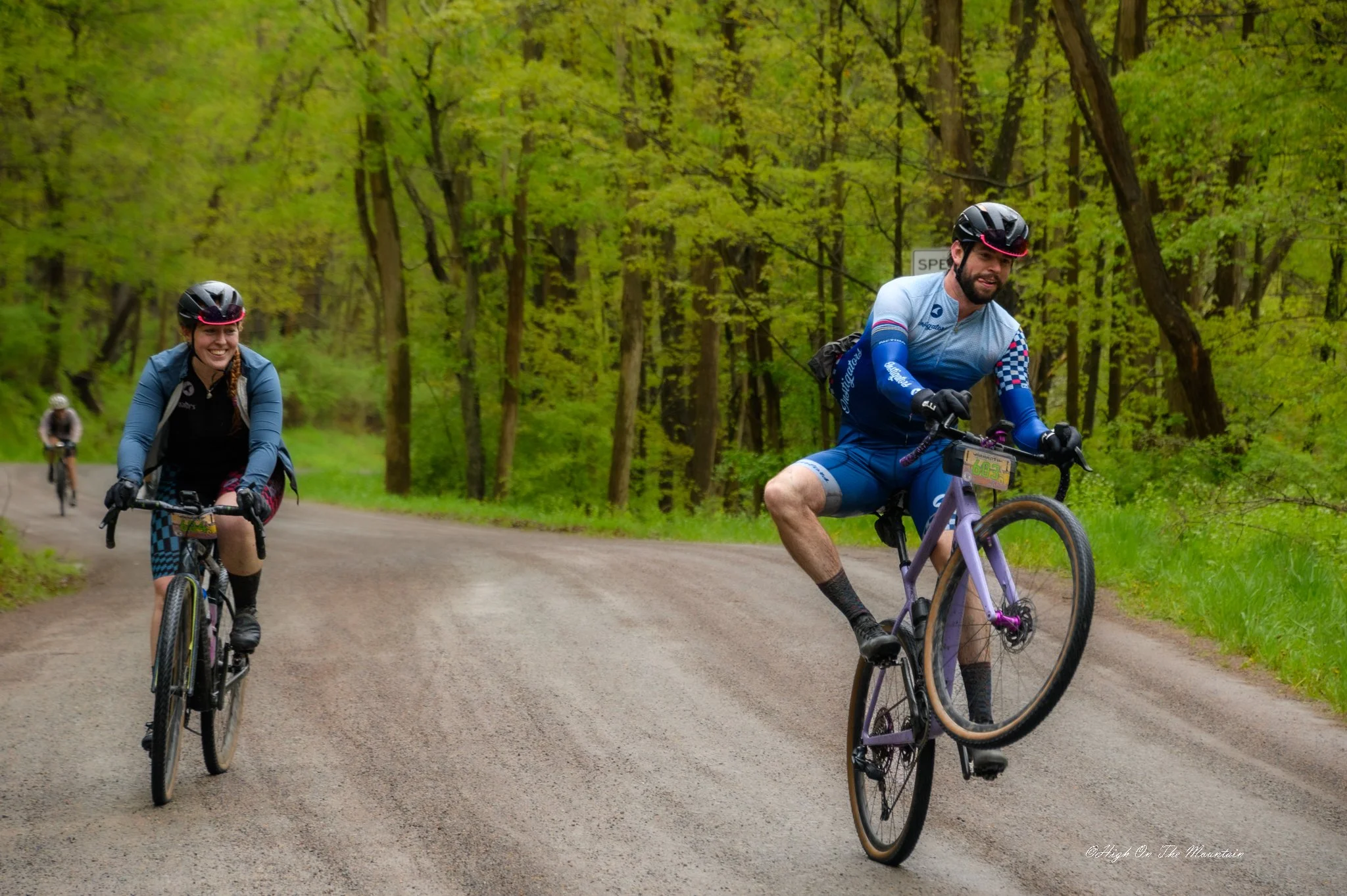 Two women and one man riding mountain bikes on a dirt trail through a lush green forest.