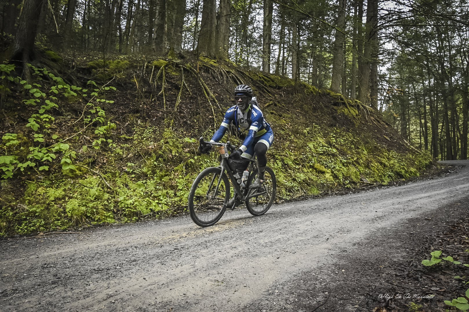 A person riding a mountain bike on a dirt trail through a wooded area with moss-covered trees and ground.