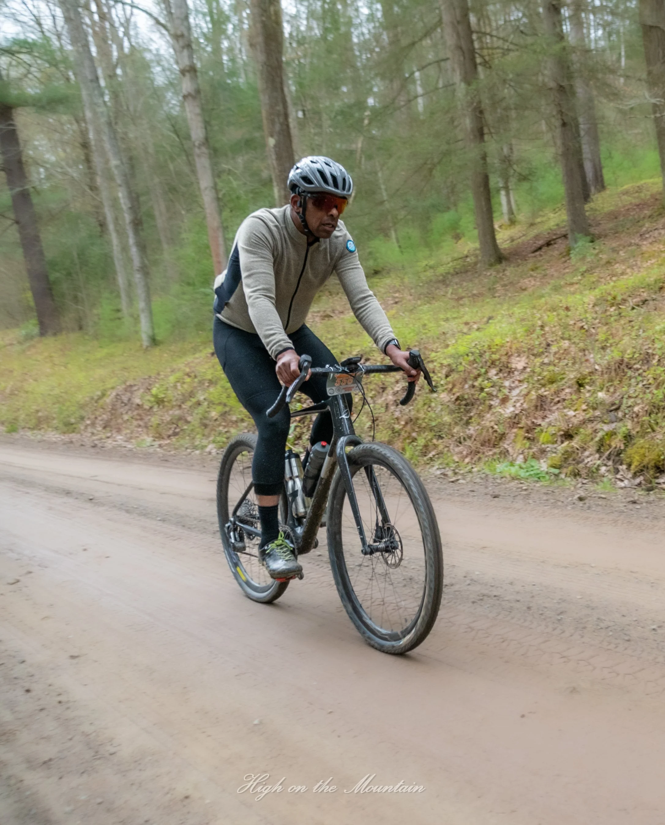 A man riding a mountain bike on a dirt trail in a forested area with tall trees and green foliage.