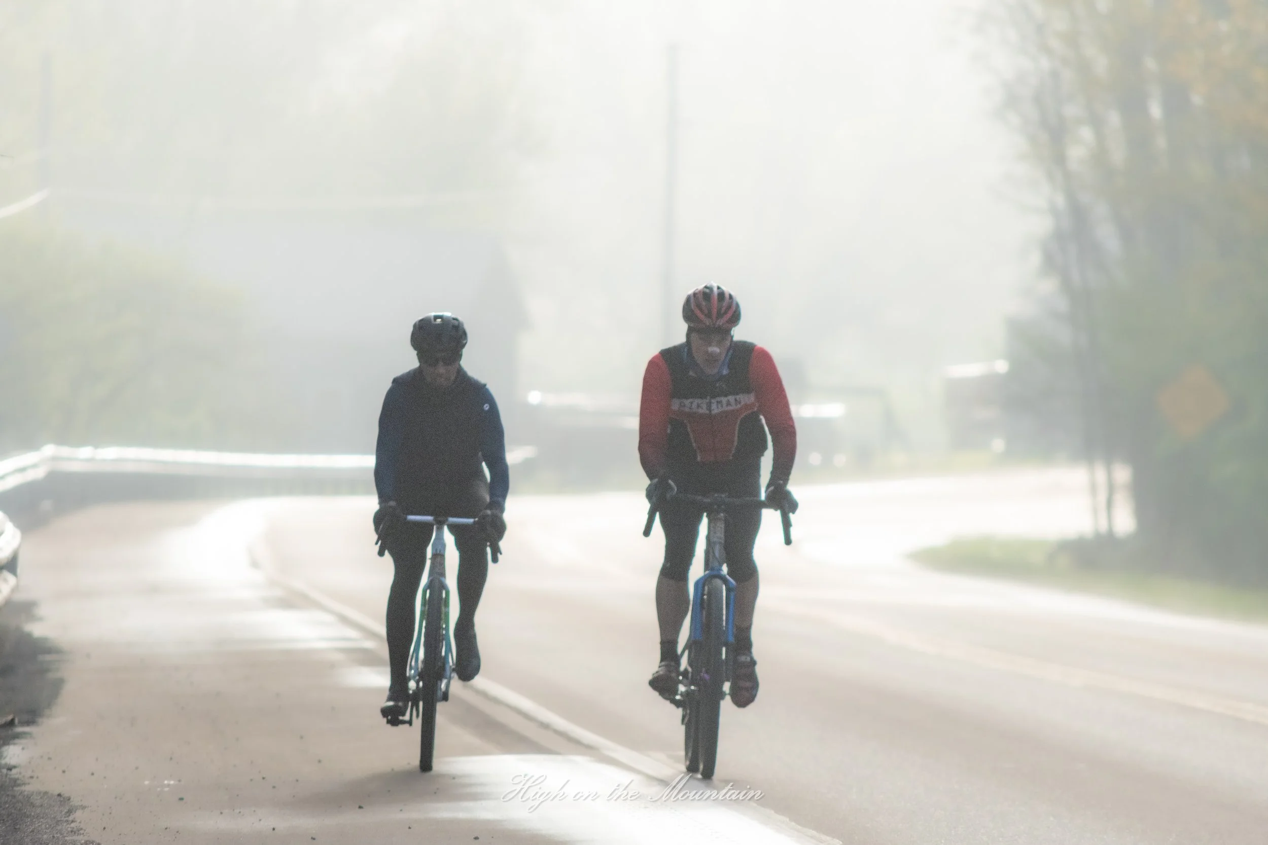 Two children riding bicycles on an early foggy morning on a quiet street.
