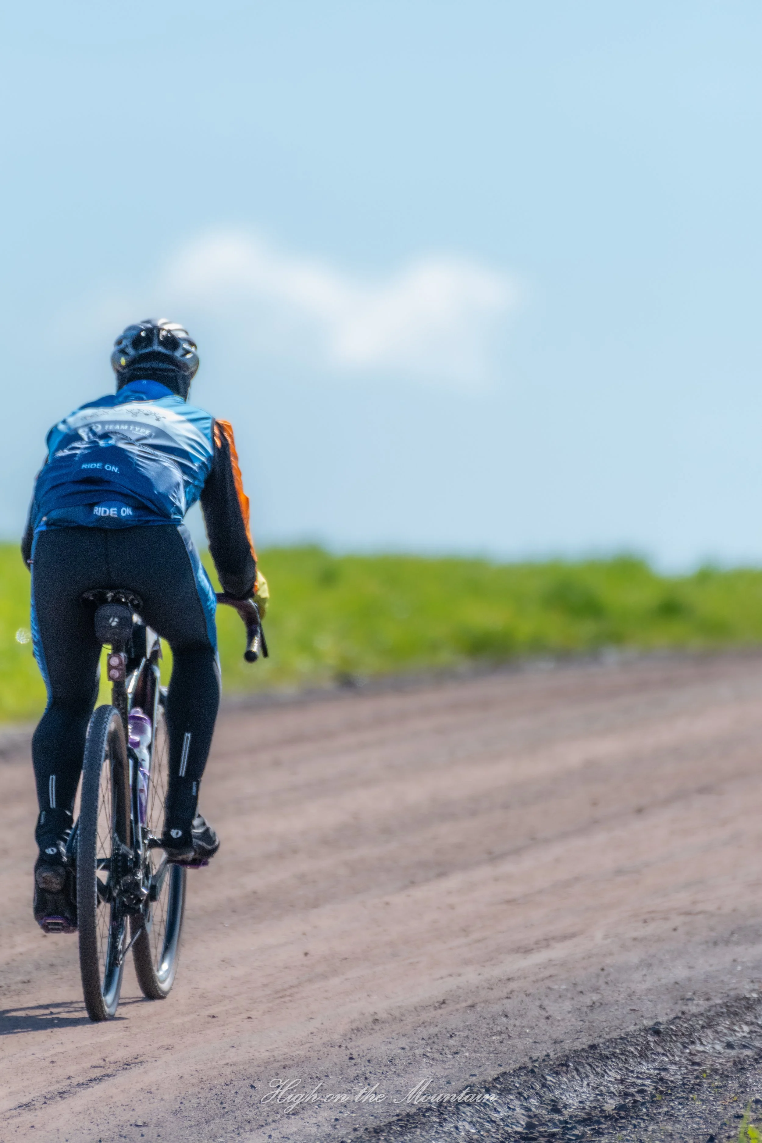 A person riding a mountain bike on a dirt trail in a mountainous area under a partly cloudy sky.