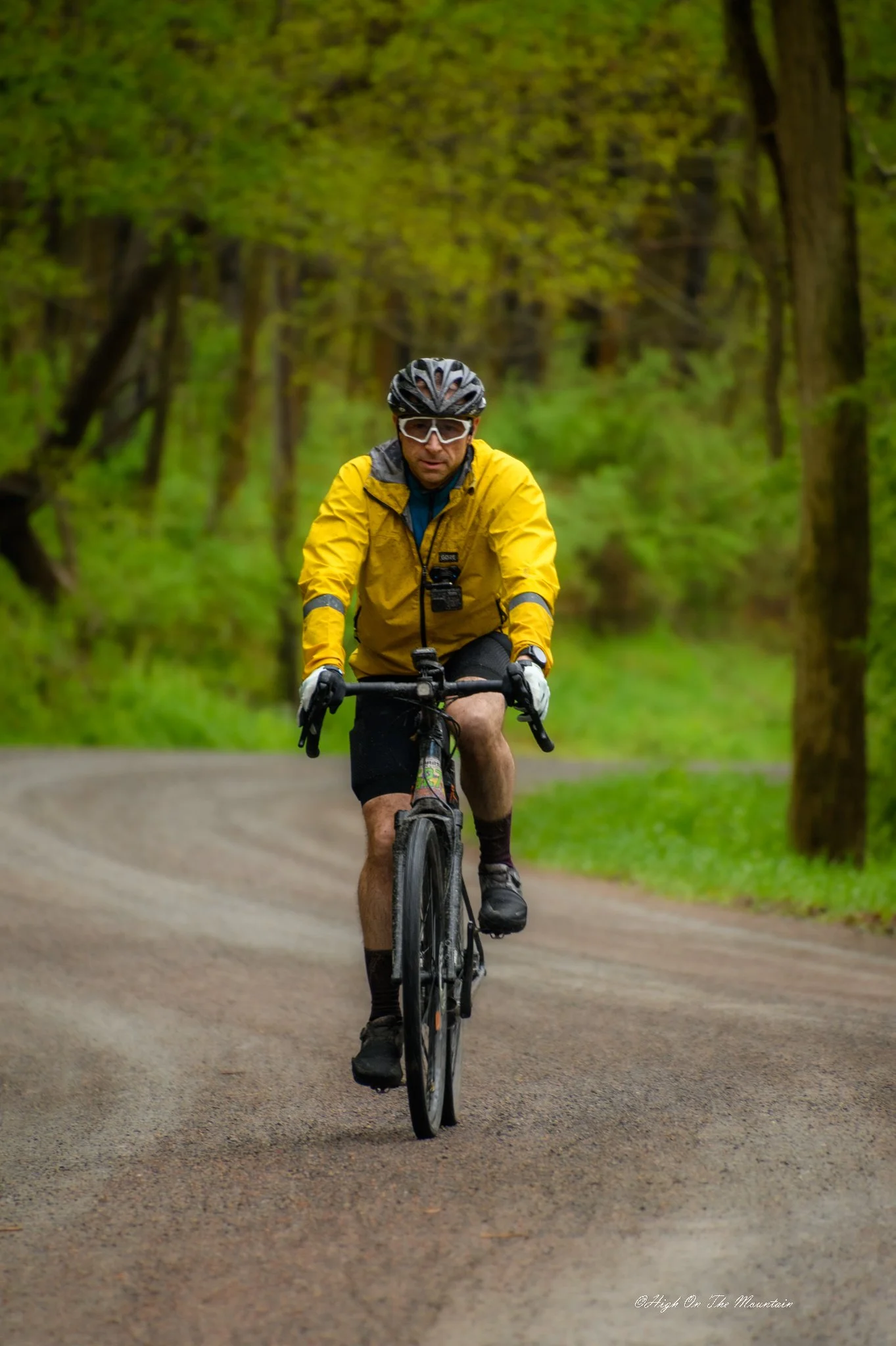 A man riding a mountain bike on a dirt trail in a forest with green trees around him.