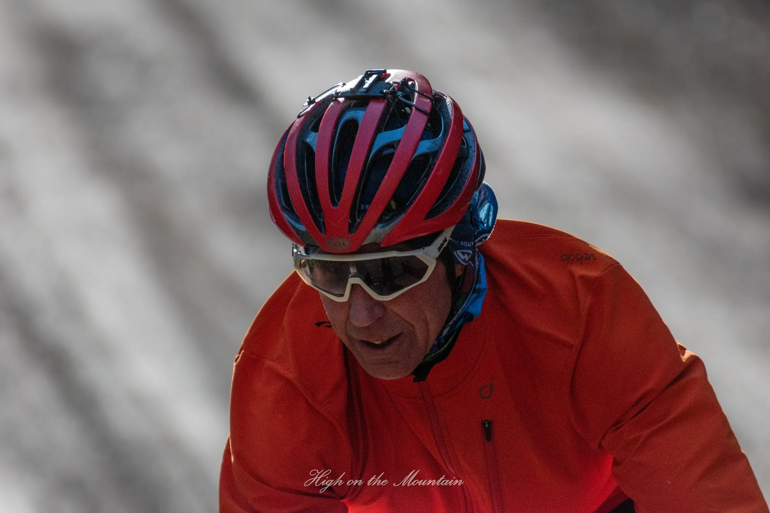 A person wearing a red helmet and matching red jacket, likely engaged in mountain biking or downhill riding, leaning forward on a trail with a blurred background indicating motion and speed.