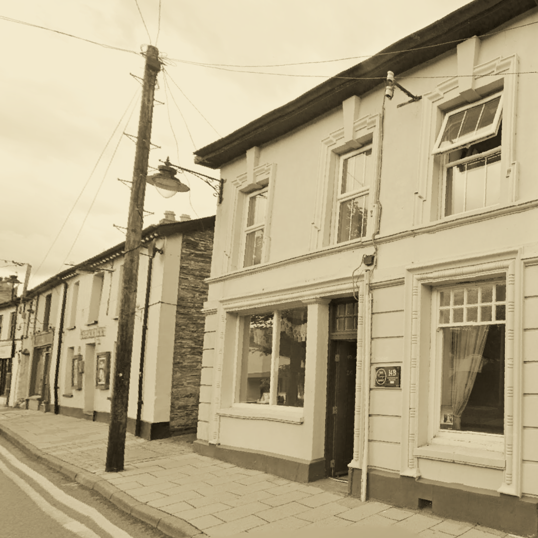 14 Sycamore Street, Newcastle Emlyn. A row of old town-style buildings with large windows and a pavement in front, and a wooden utility pole with multiple wires attached.