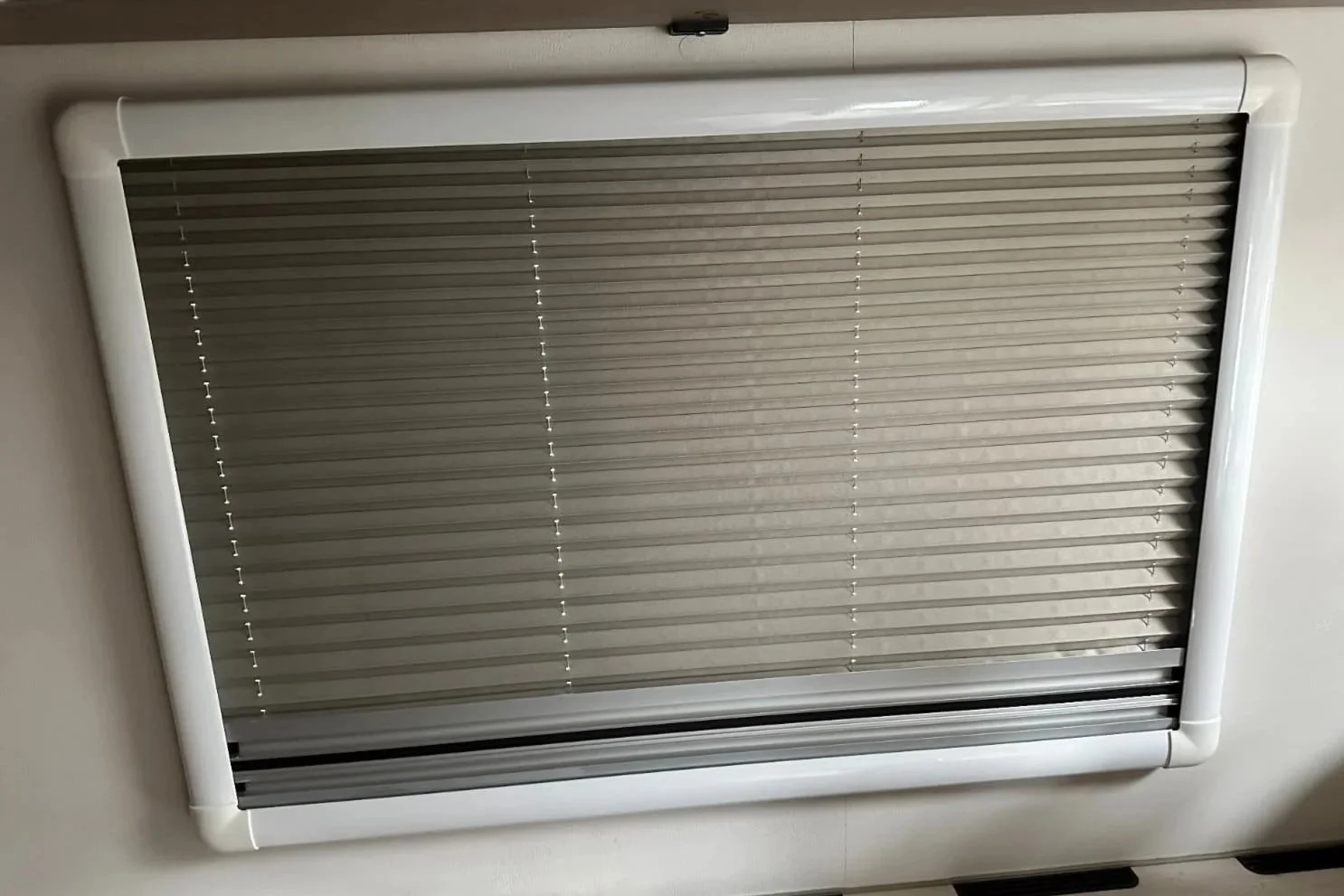 A closed window with beige horizontal blinds framed by white plastic trims.