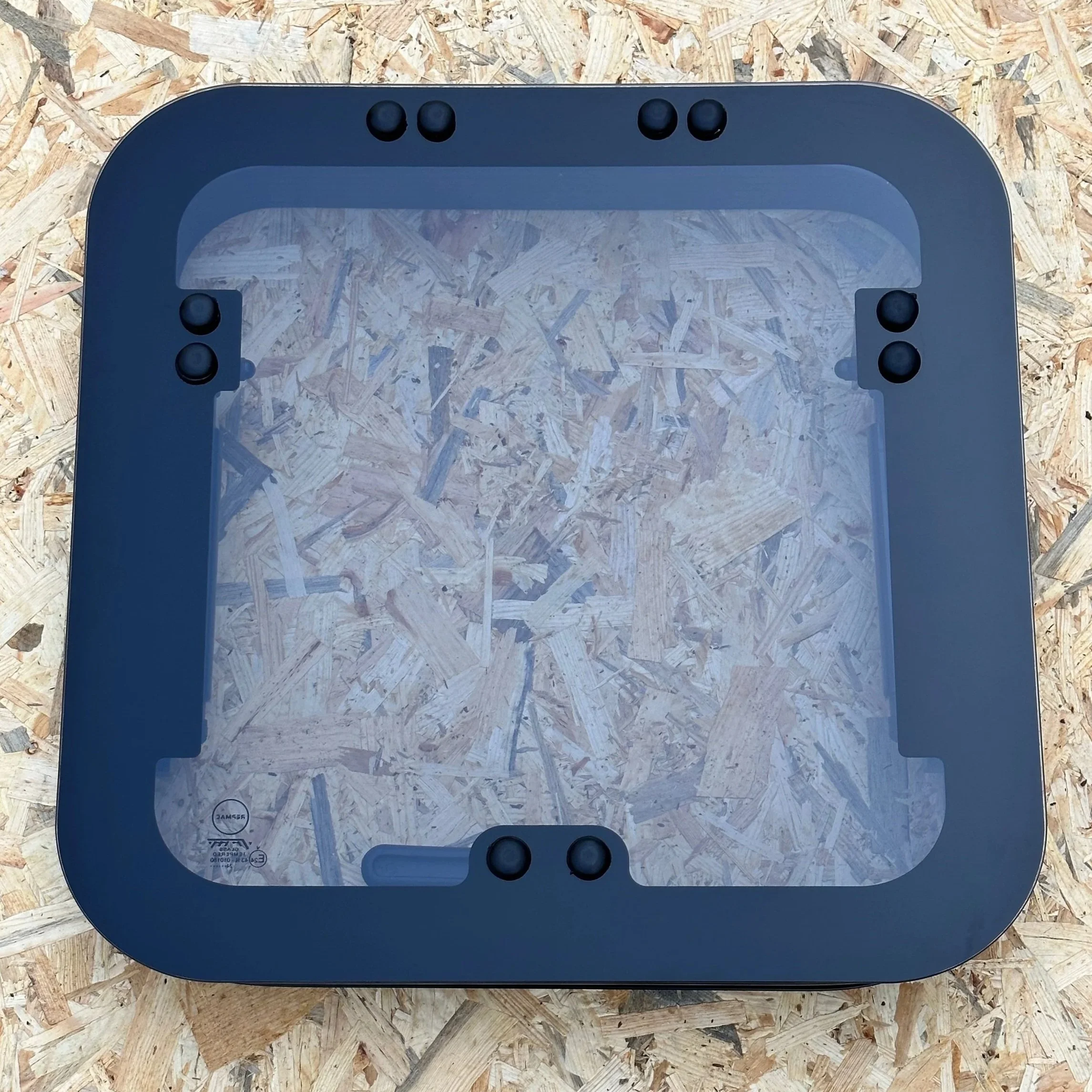 A square black frame with rounded corners and four rubber feet on a wooden surface.