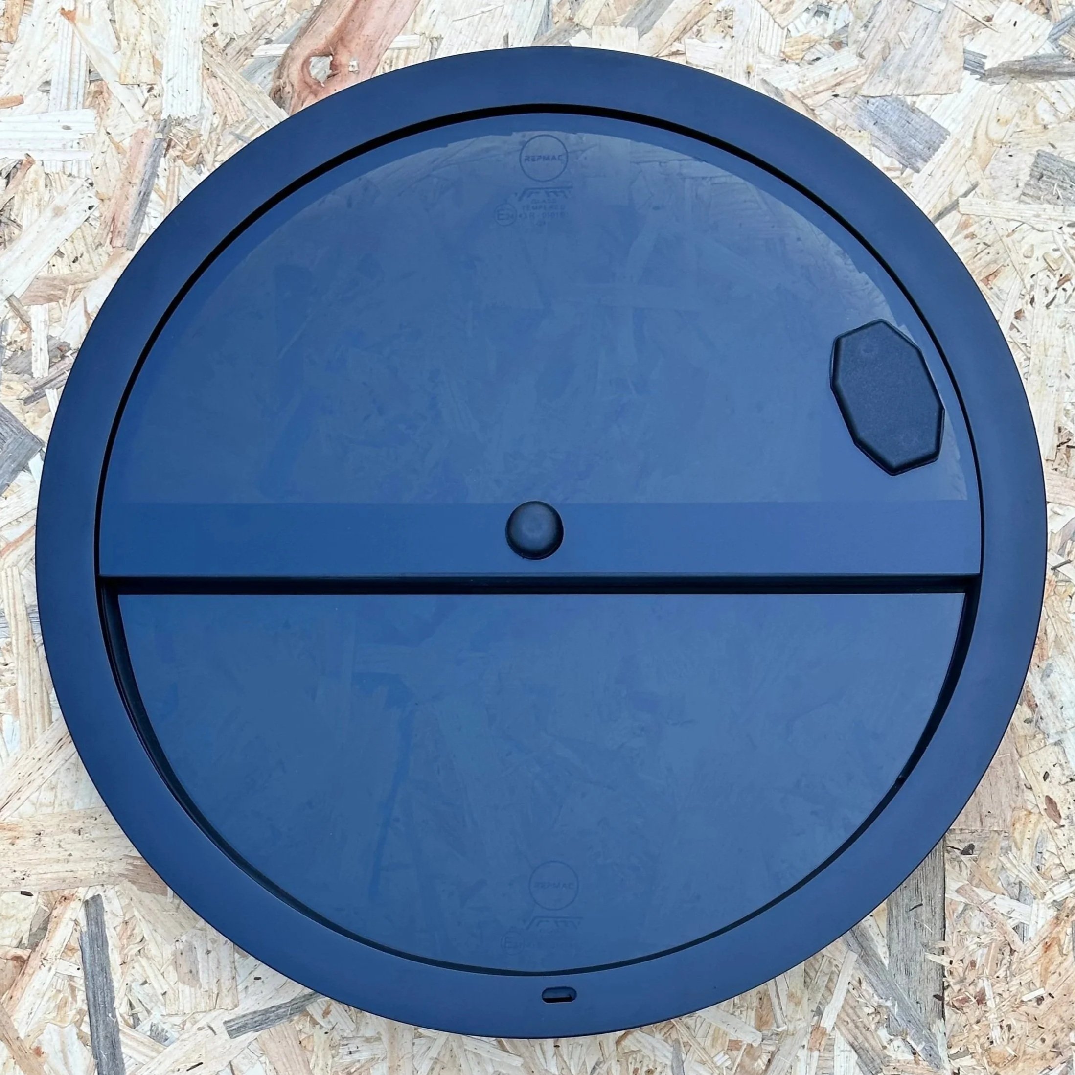A round, black device with a small hexagonal handle on the upper right side, lying on a wooden surface.