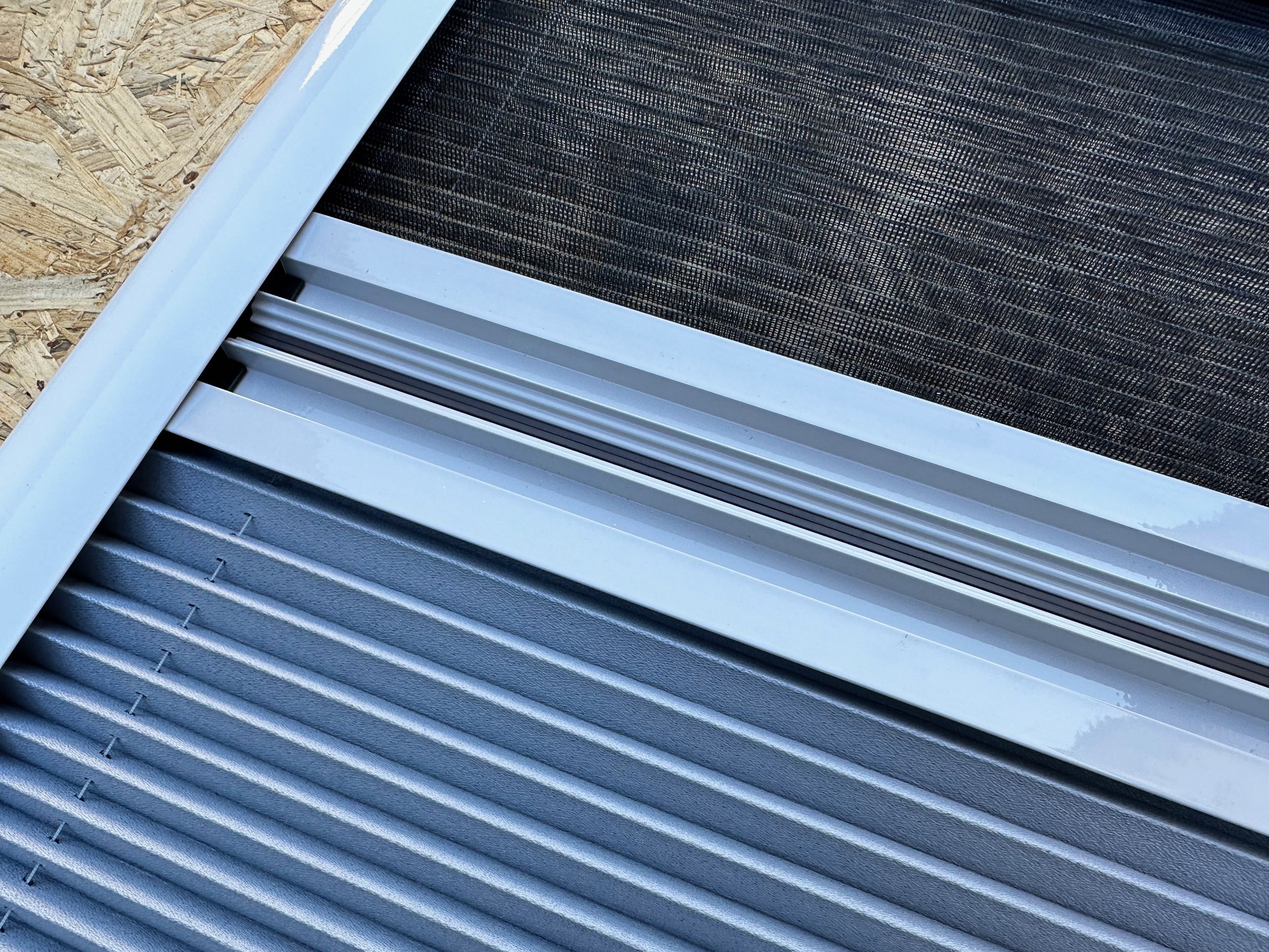 Close-up of air conditioning or heating unit vents with metallic and plastic components installed on plywood.