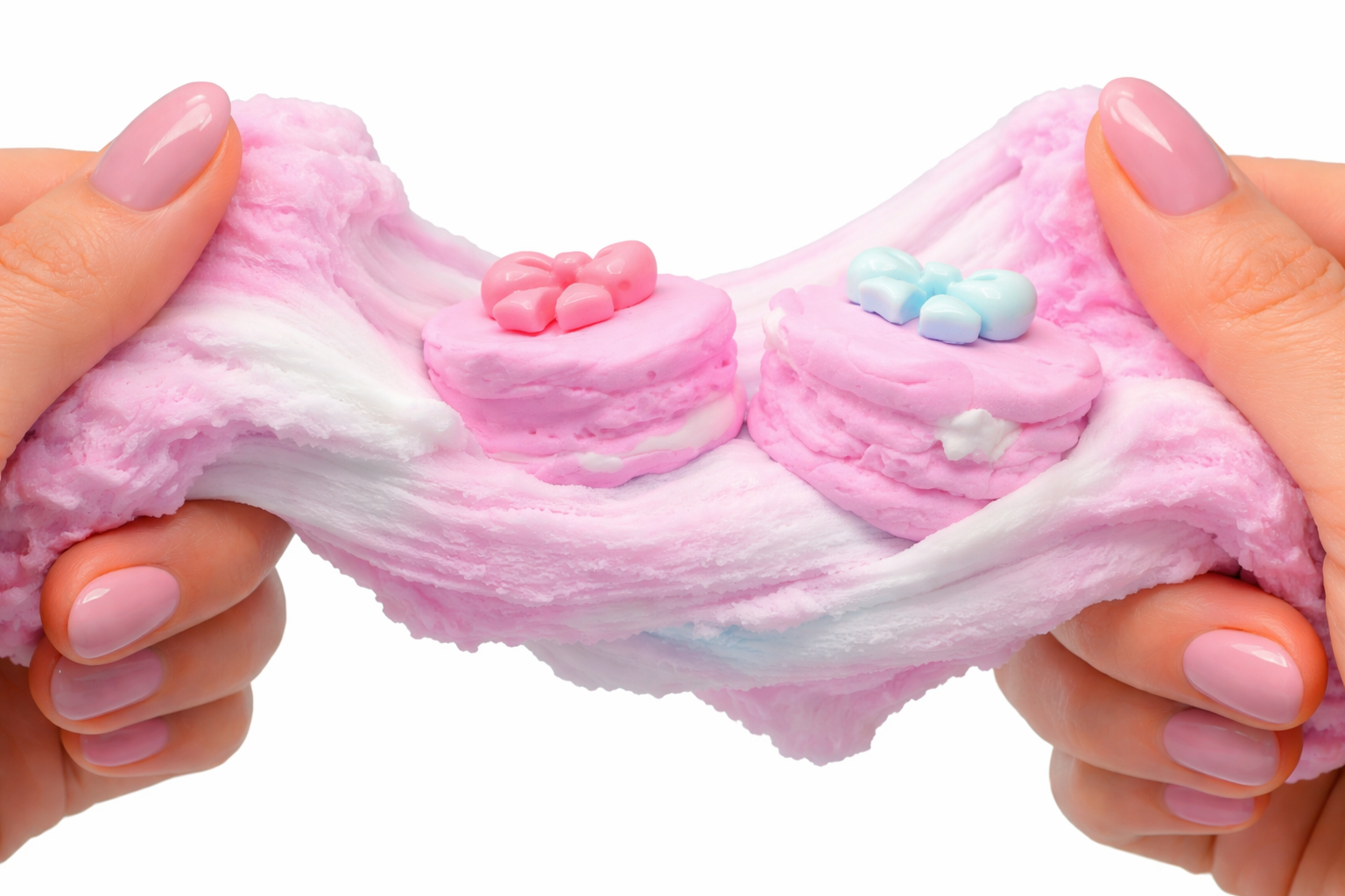 Close-up of hands stretching a pink slime with small plastic fruit and candy decorations, including a pineapple, strawberry, banana, and lemon, over a pastel pink background.