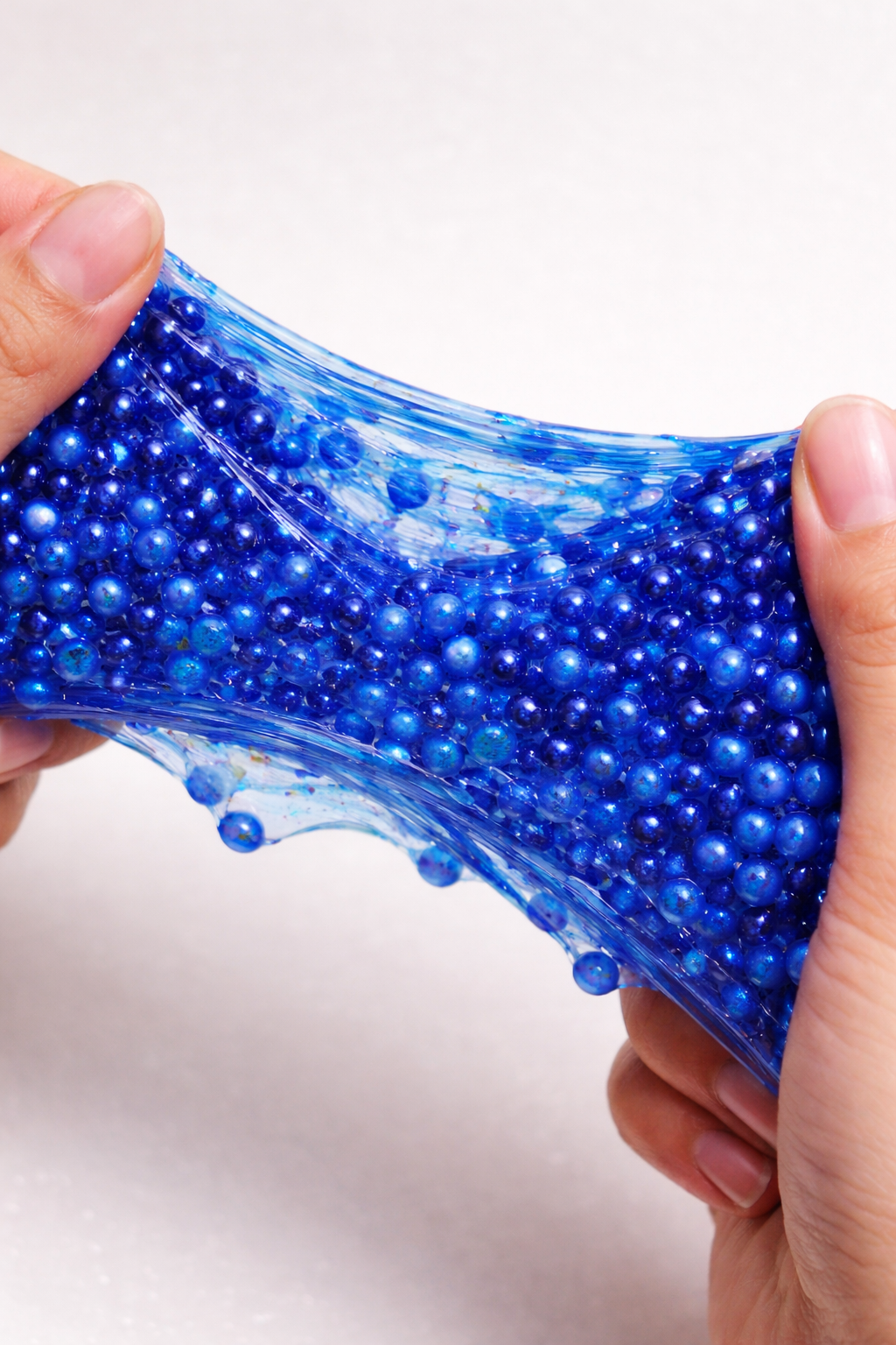 Hands stretching blue slime with small blue beads inside.