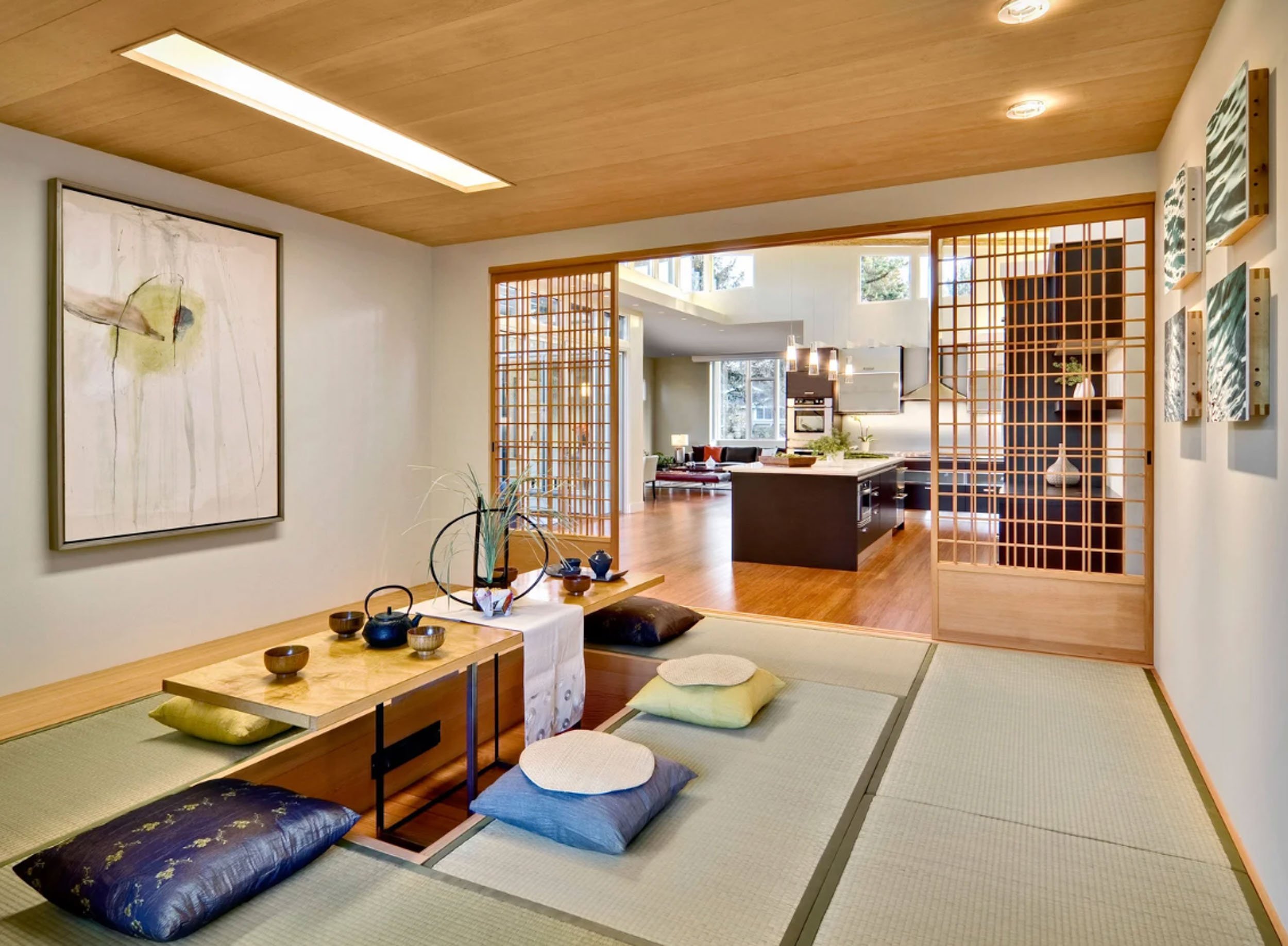 A large gestural abstract painting and a vertical series of smaller framed works bring modern art into a traditional Japanese tatami room with low wooden tables and floor cushions on the mats.