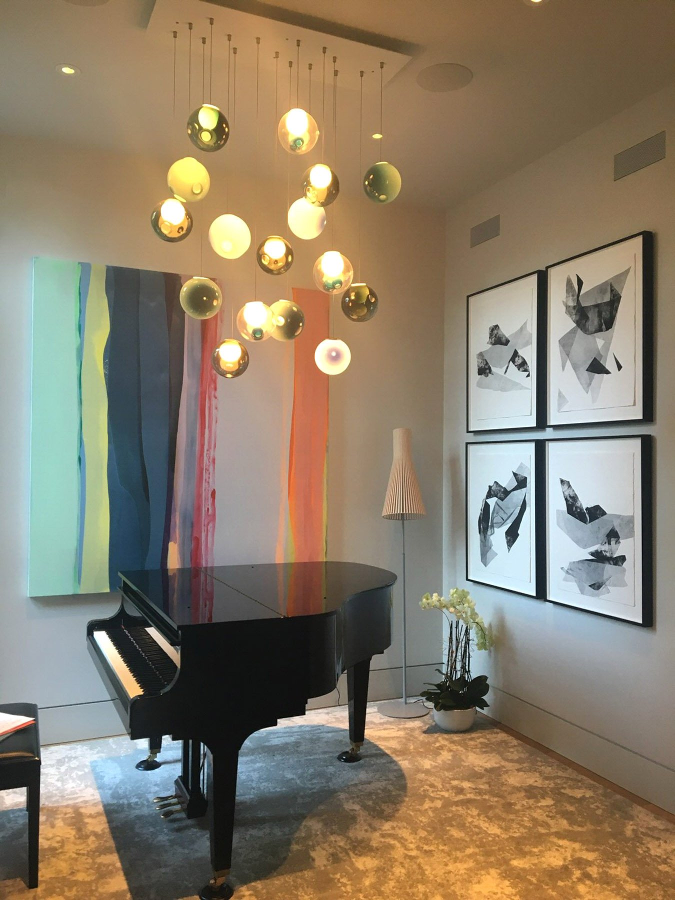 A bold vertical-striped abstract painting in teal, blue, green, and orange behind a grand piano, with four black-and-white abstract works grouped on the adjacent wall.