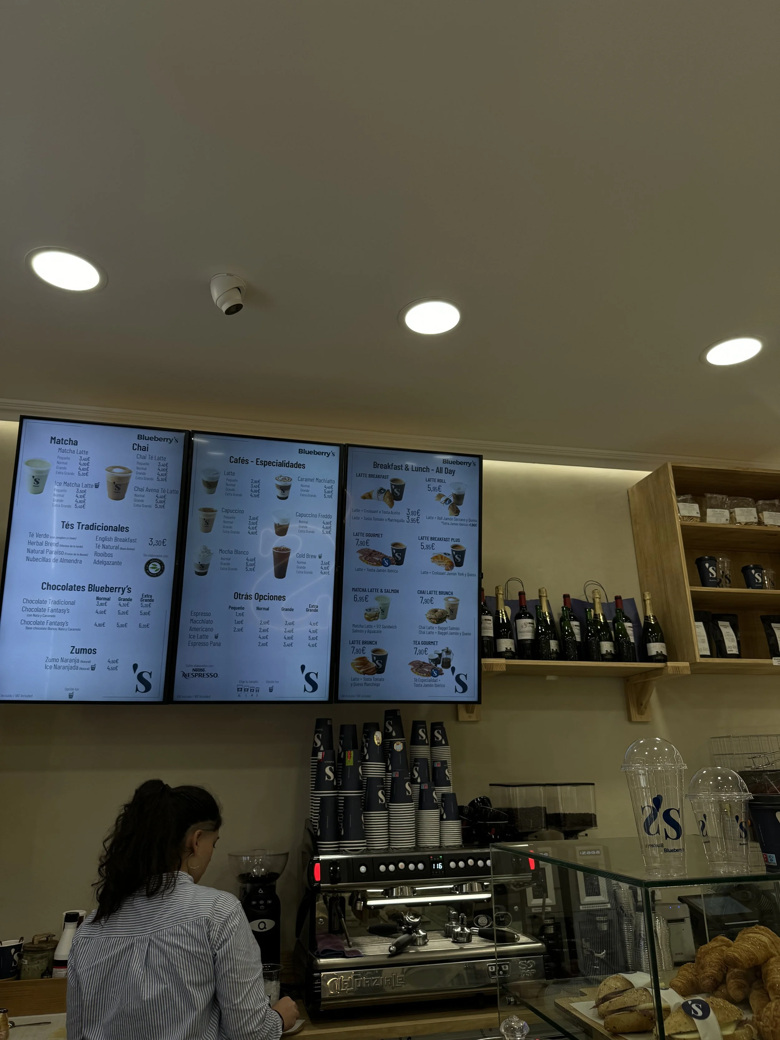 Menu screen displaying different coffee options and prices at Blueberry's café, with a barista preparing drinks behind the counter.