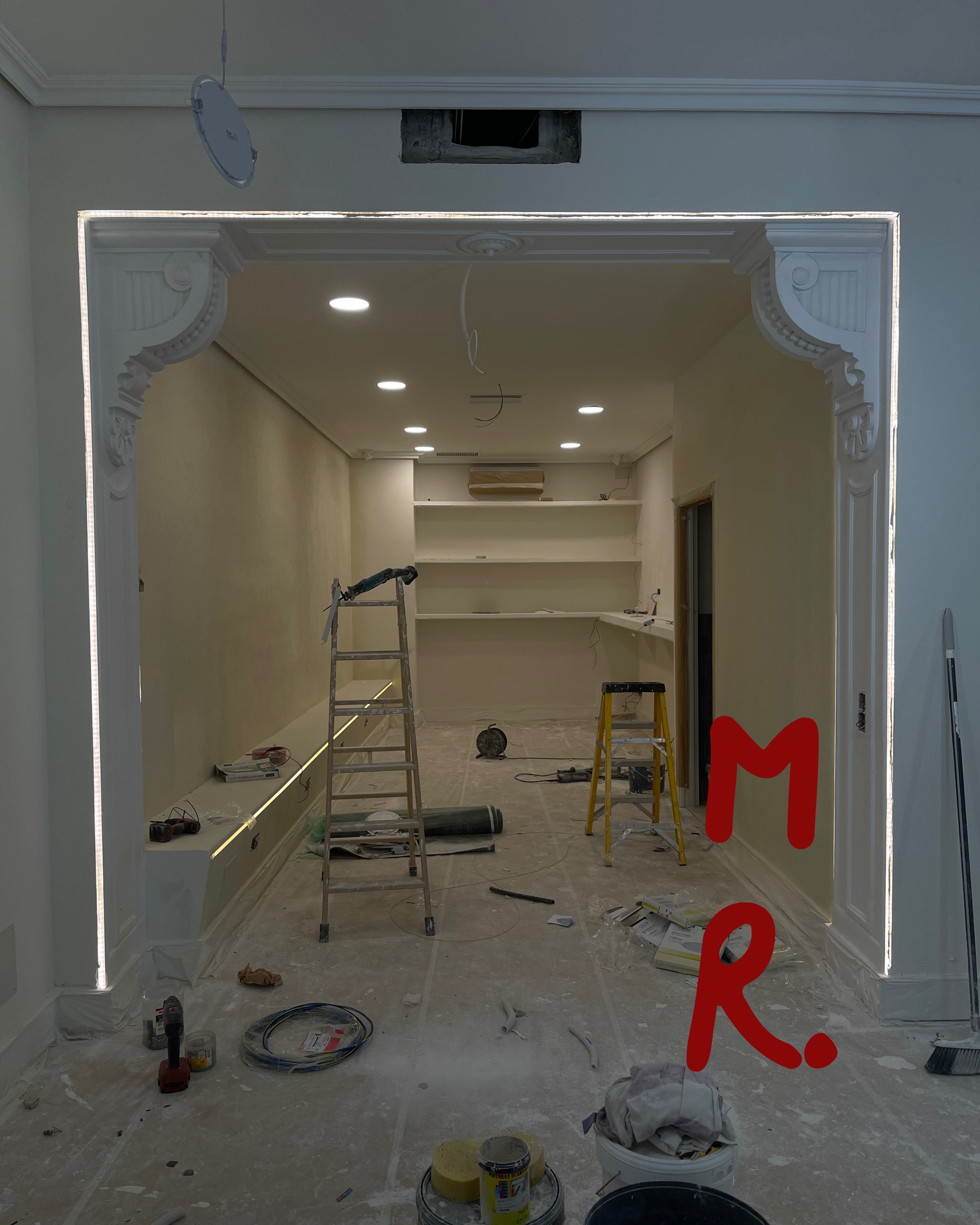 Interior room under renovation with ladders, construction tools, and unfinished details, including built-in shelves and decorative architectural moldings.