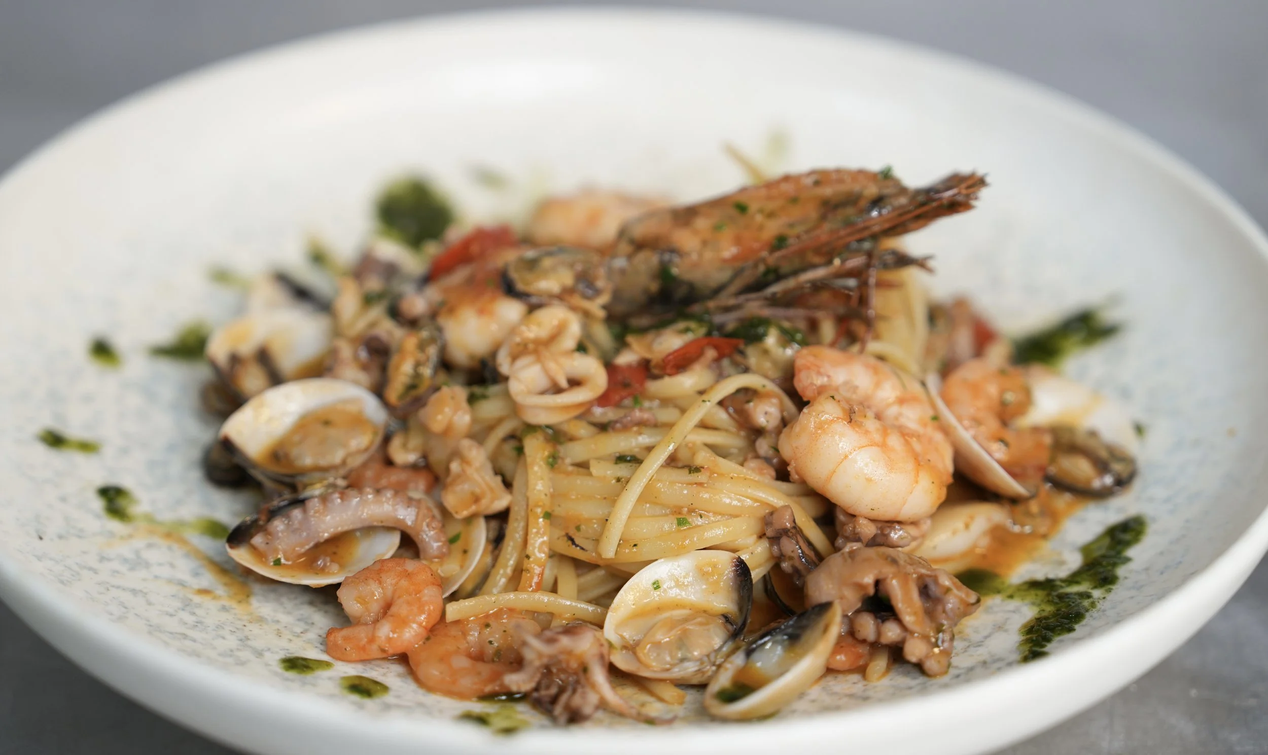 Plate of seafood pasta with shrimp, clams, squid, and herbs in a creamy sauce.
