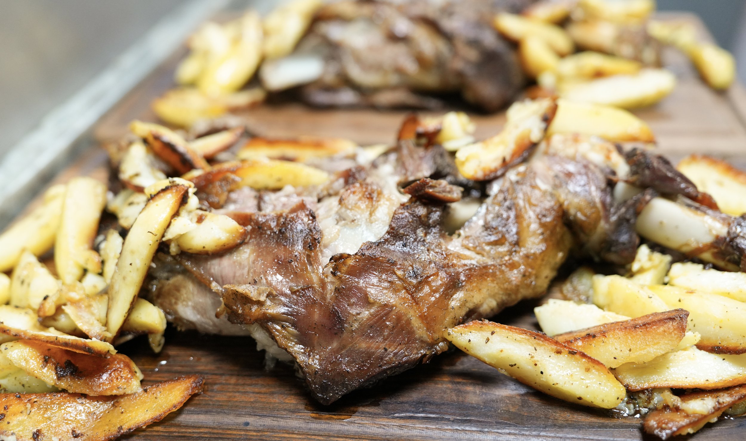 Roasted lamb with roasted potatoes on a wooden platter.
