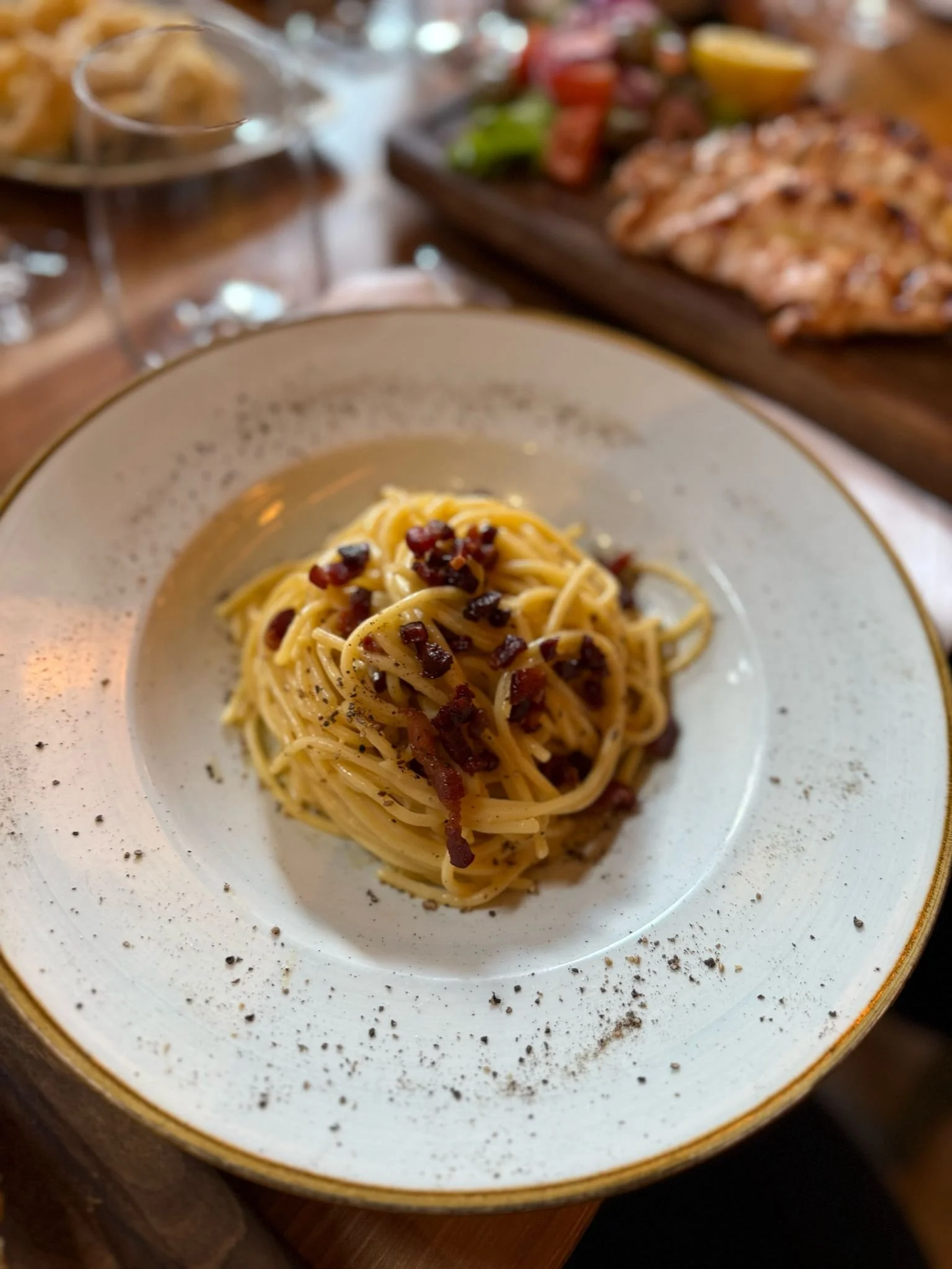 Plate of spaghetti carbonara with bacon and black pepper, served on a white plate with blurring in the background.