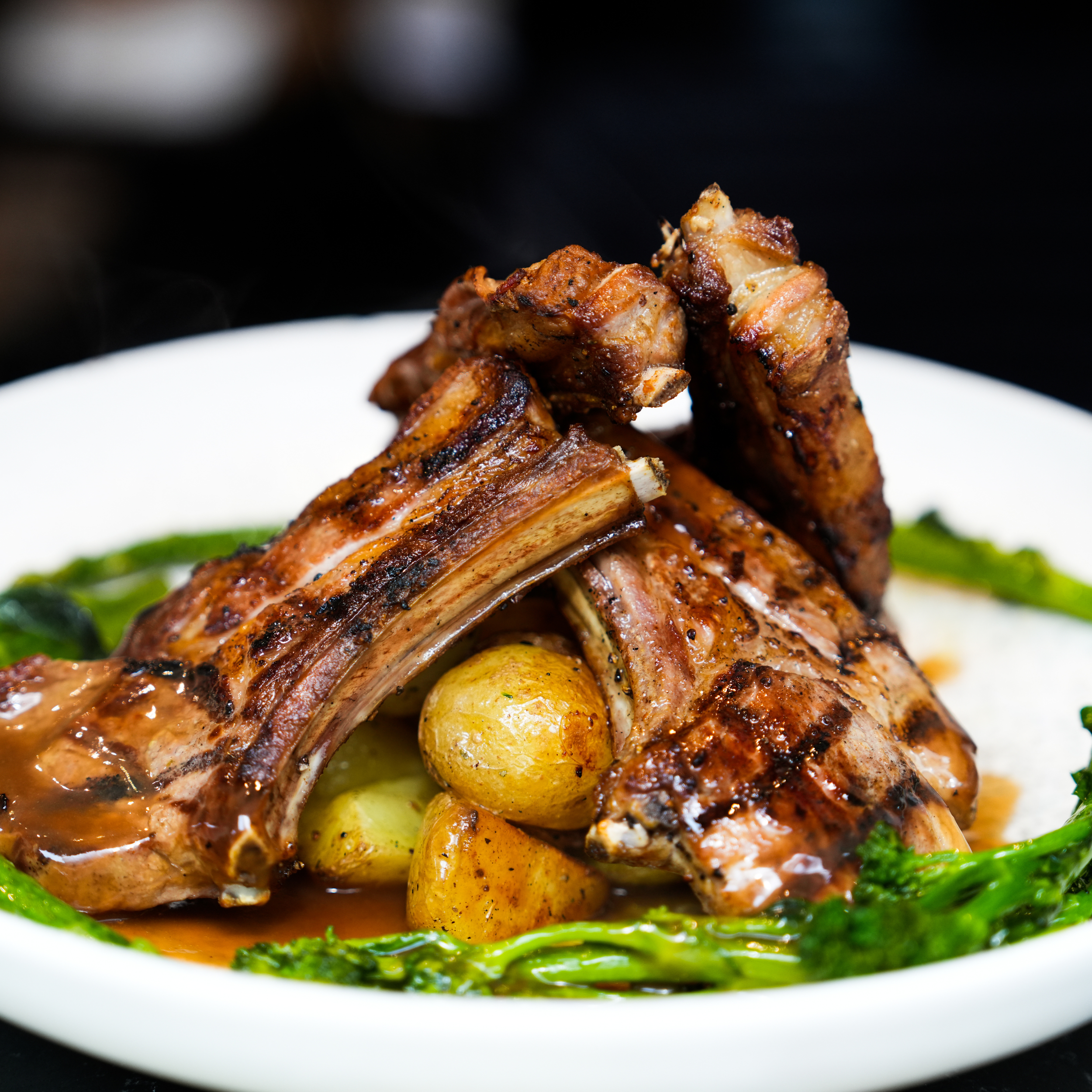 Grilled lamb chops on a plate with roasted potatoes, green vegetables, and sauce.