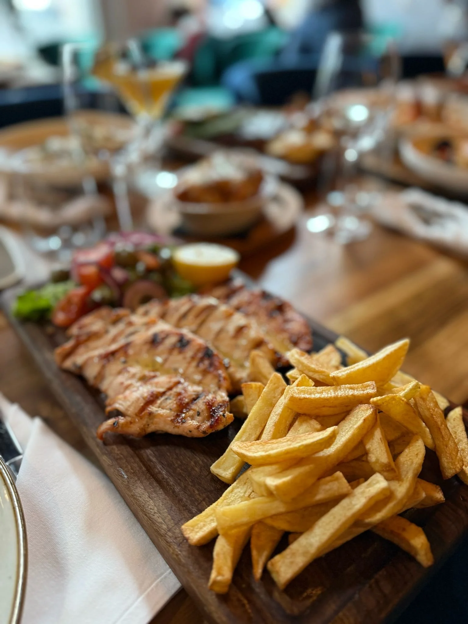Grilled chicken with fries and vegetables on a wooden platter