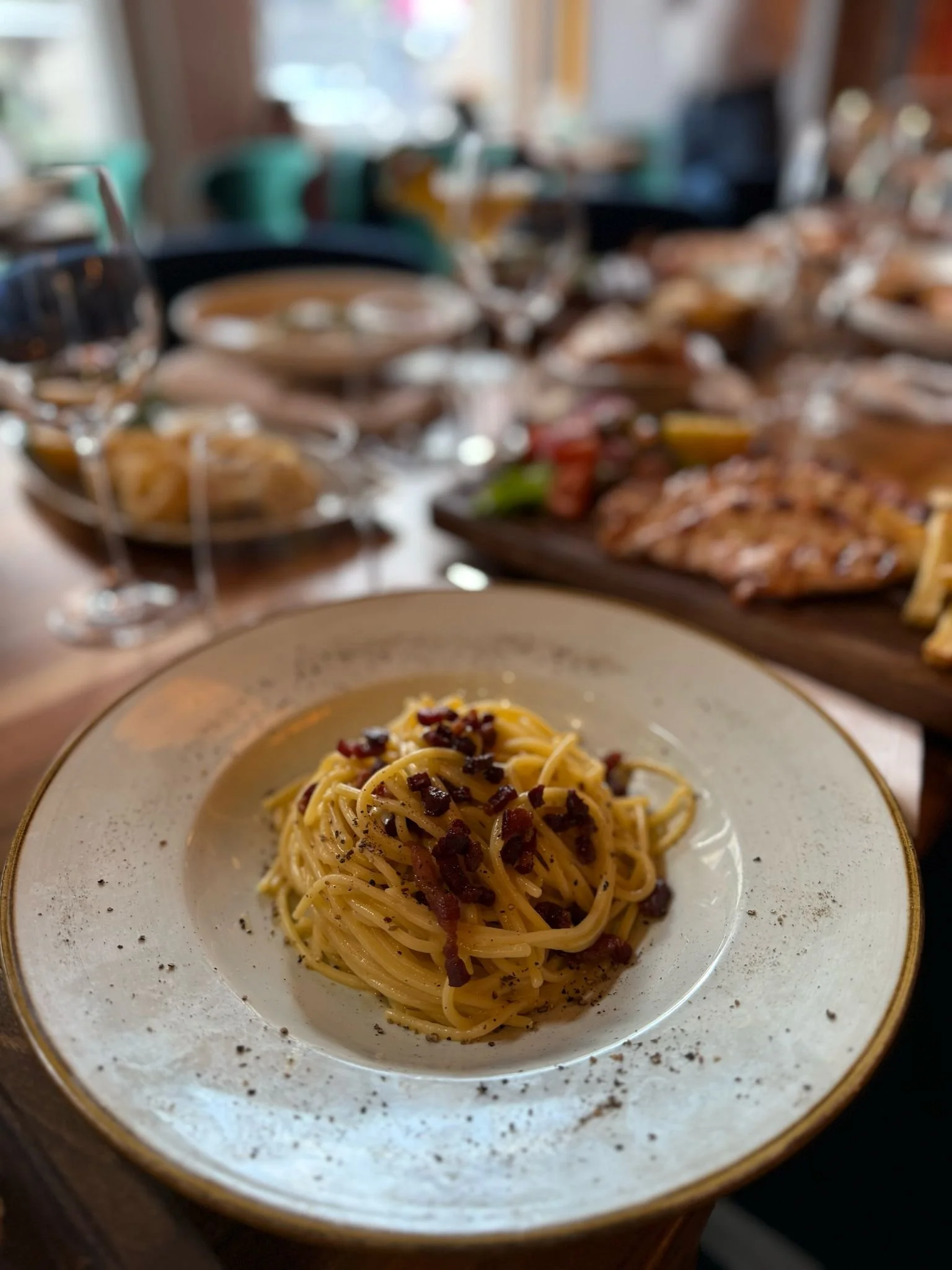 Plate of spaghetti carbonara with bacon and pepper on a dining table.
