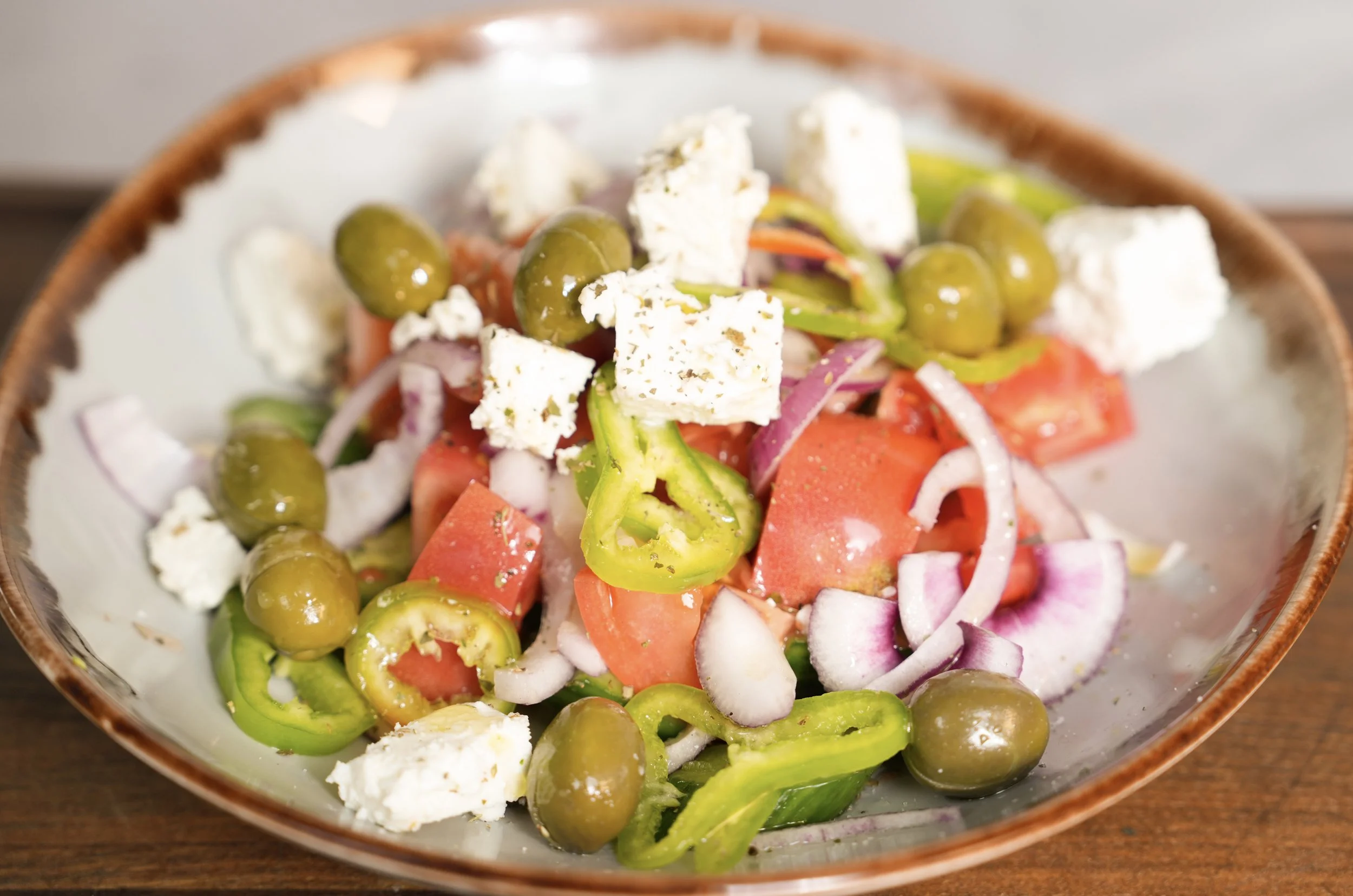 Greek salad with tomatoes, feta cheese, olives, red onions, and green bell peppers in a bowl.