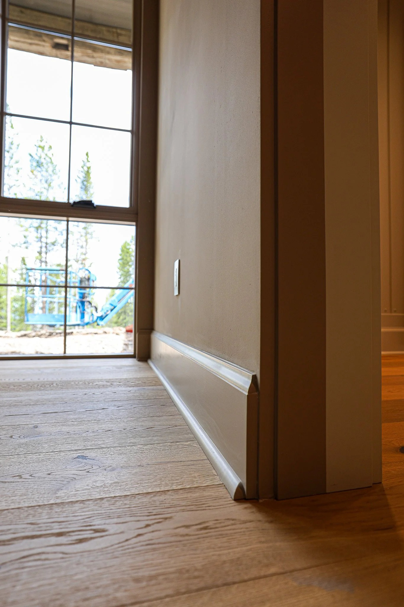 A view of hardwood flooring next to a beige wall with baseboard and a window showing a playground outside.