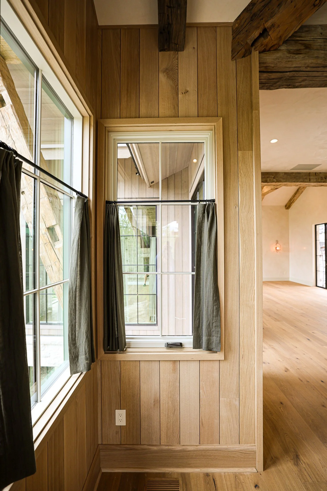 Interior of a room with wooden walls and flooring, featuring a window with curtains and a door with glass panes leading outside.