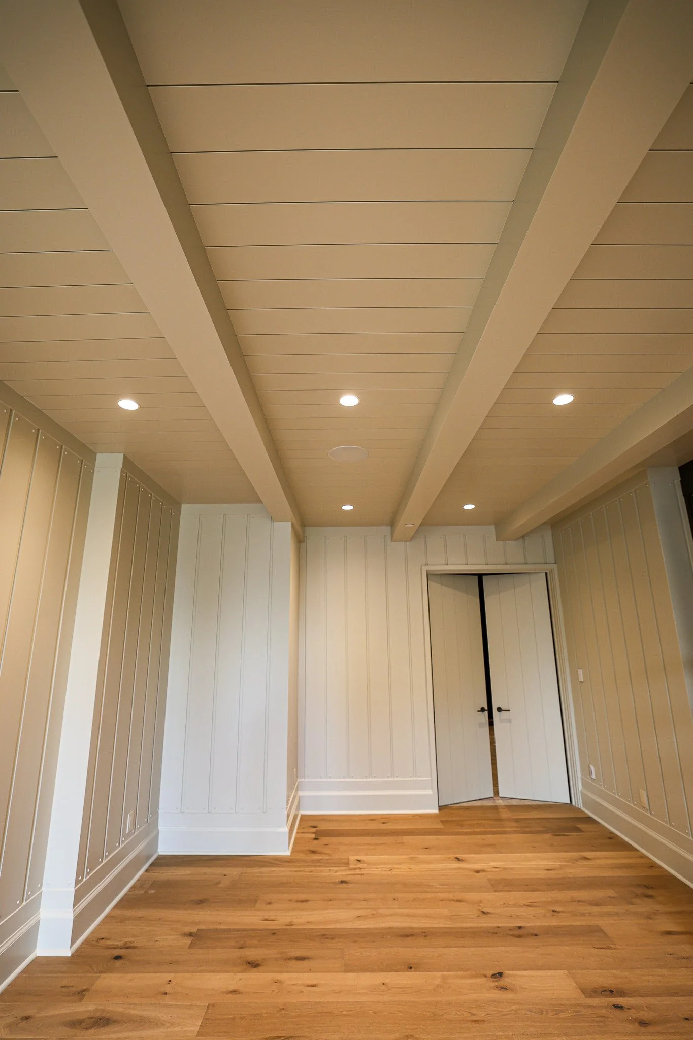 Interior view of a room with beige paneled walls, wooden flooring, a white door, and a textured ceiling with recessed lighting.