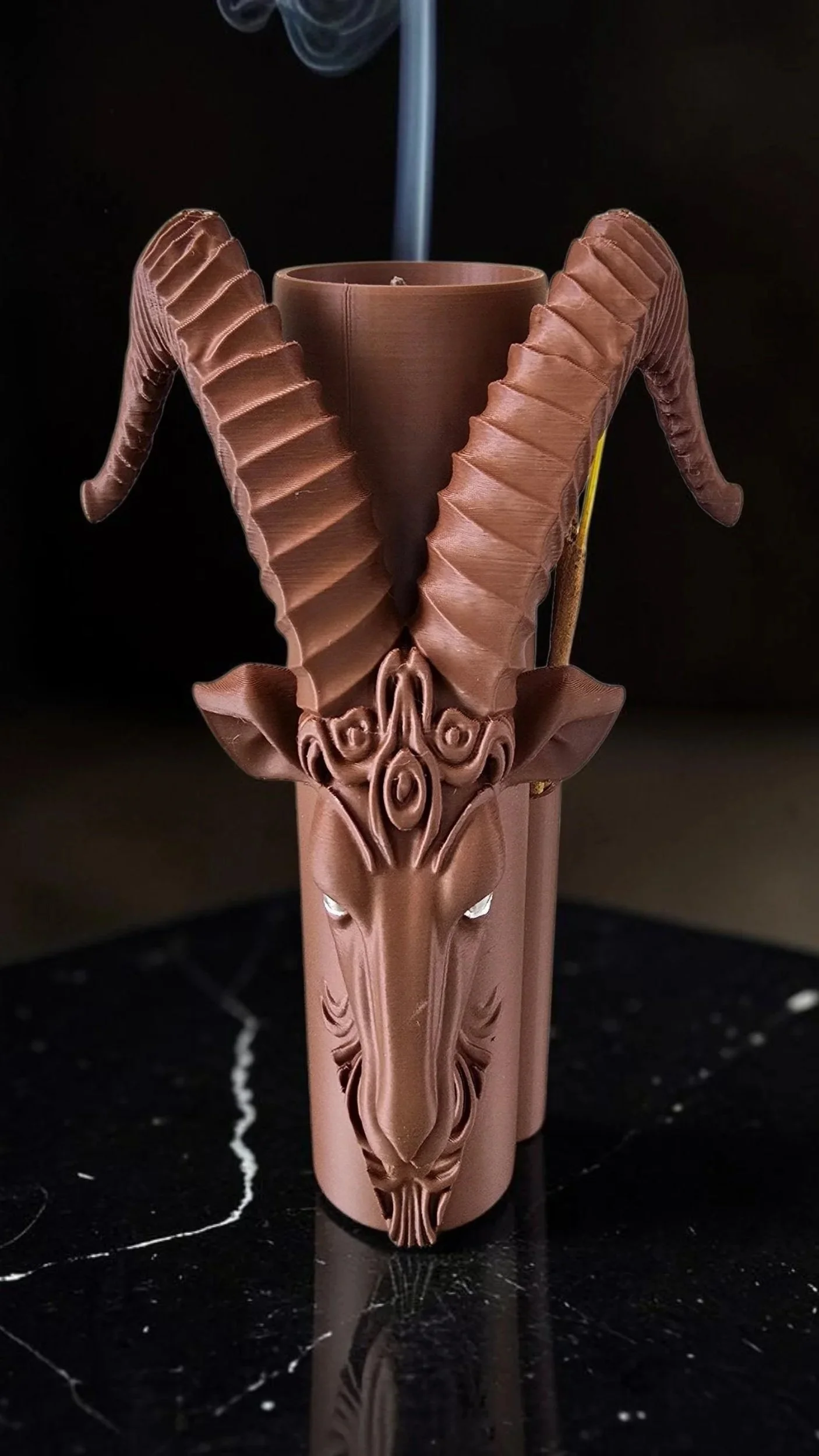 A decorative brown Incense stick holder, design of an animal skull with large, curved horns.