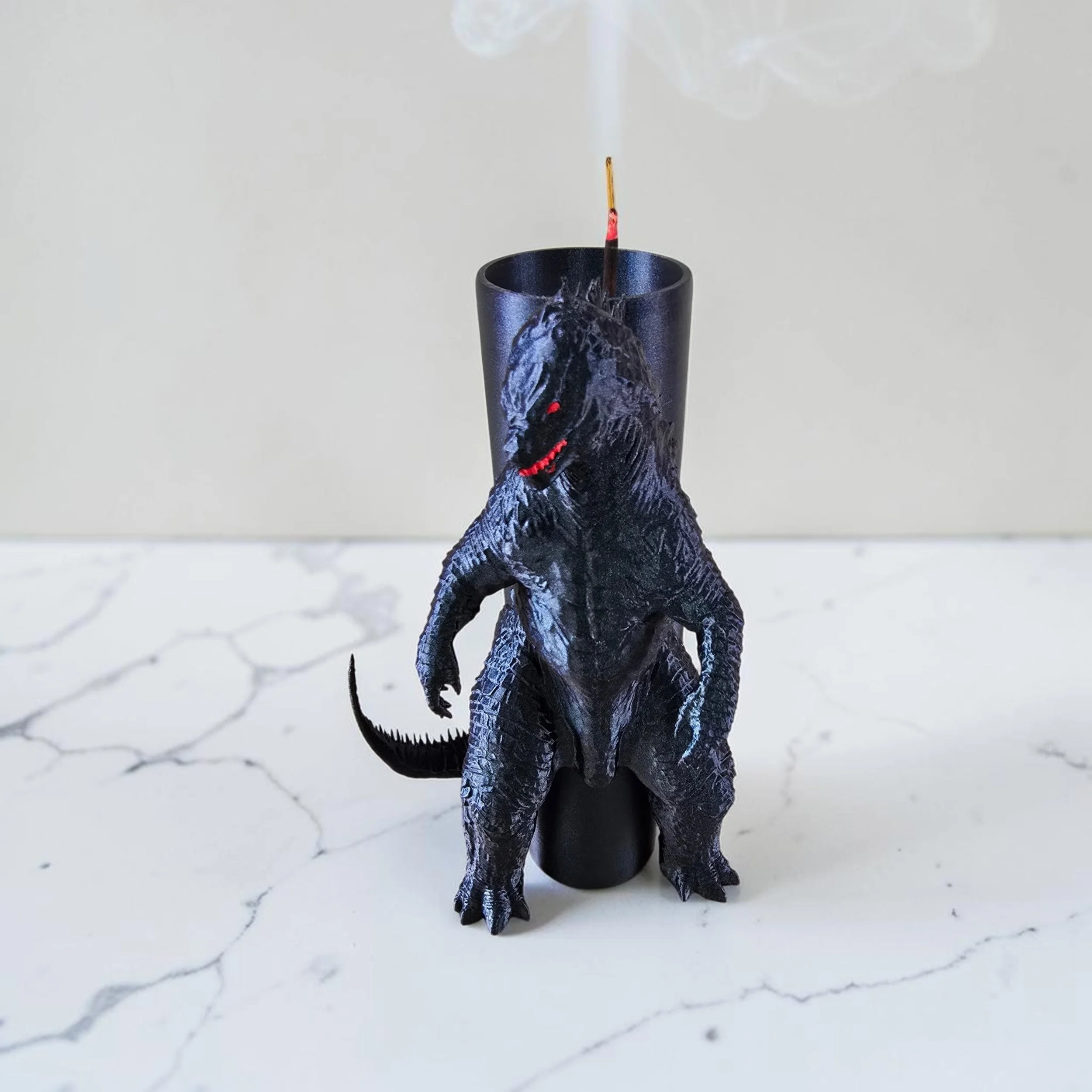 A 3D printed Tyrannosaurus rex toy Incense stick holder, black and gray with red accents, standing on a white marble surface with faint gray veining.