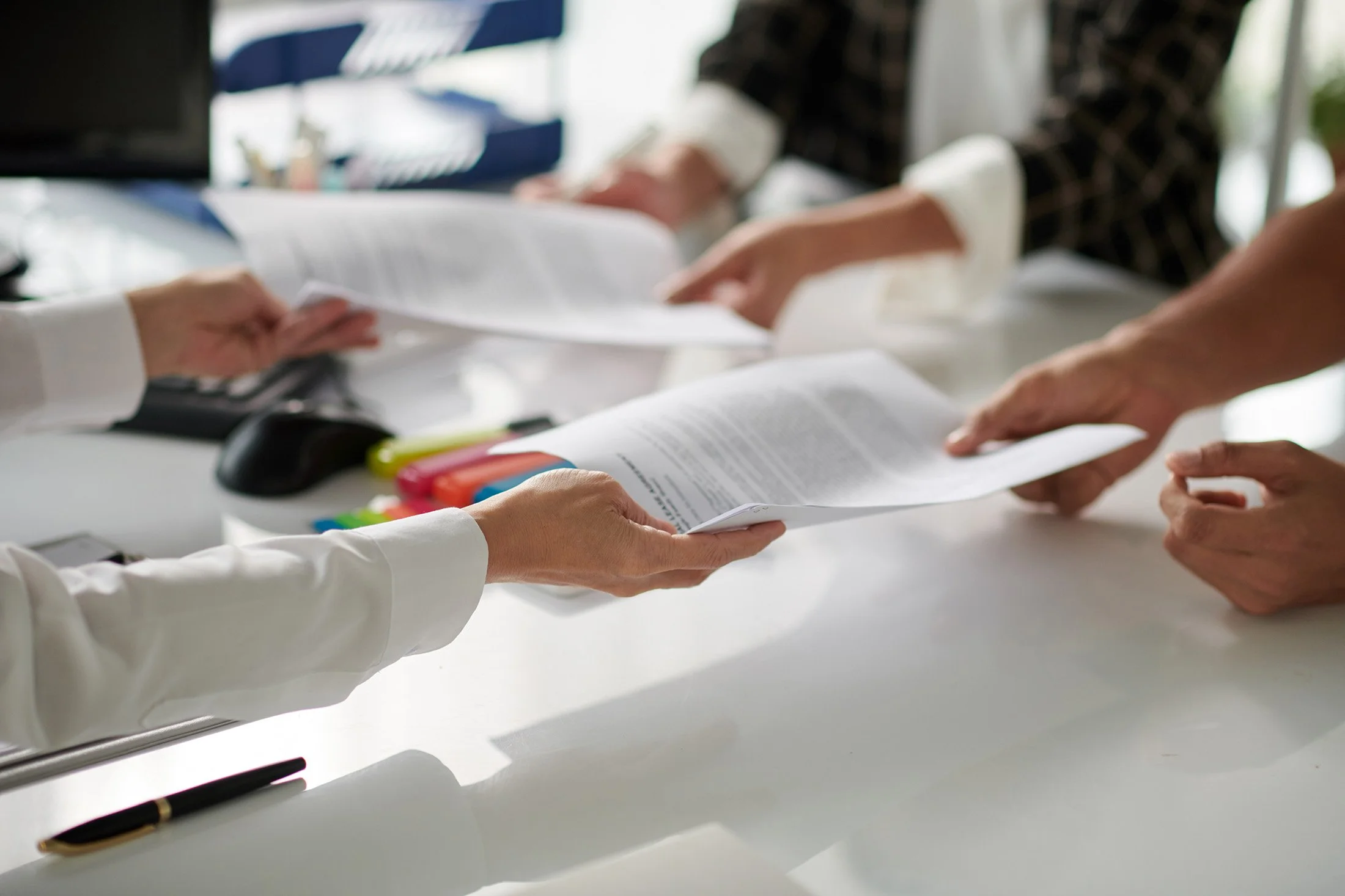 Employer and employee exchanging documents at a conference table with a mediator present — illustrating professional resolution of workplace conflicts through ADR in Colorado