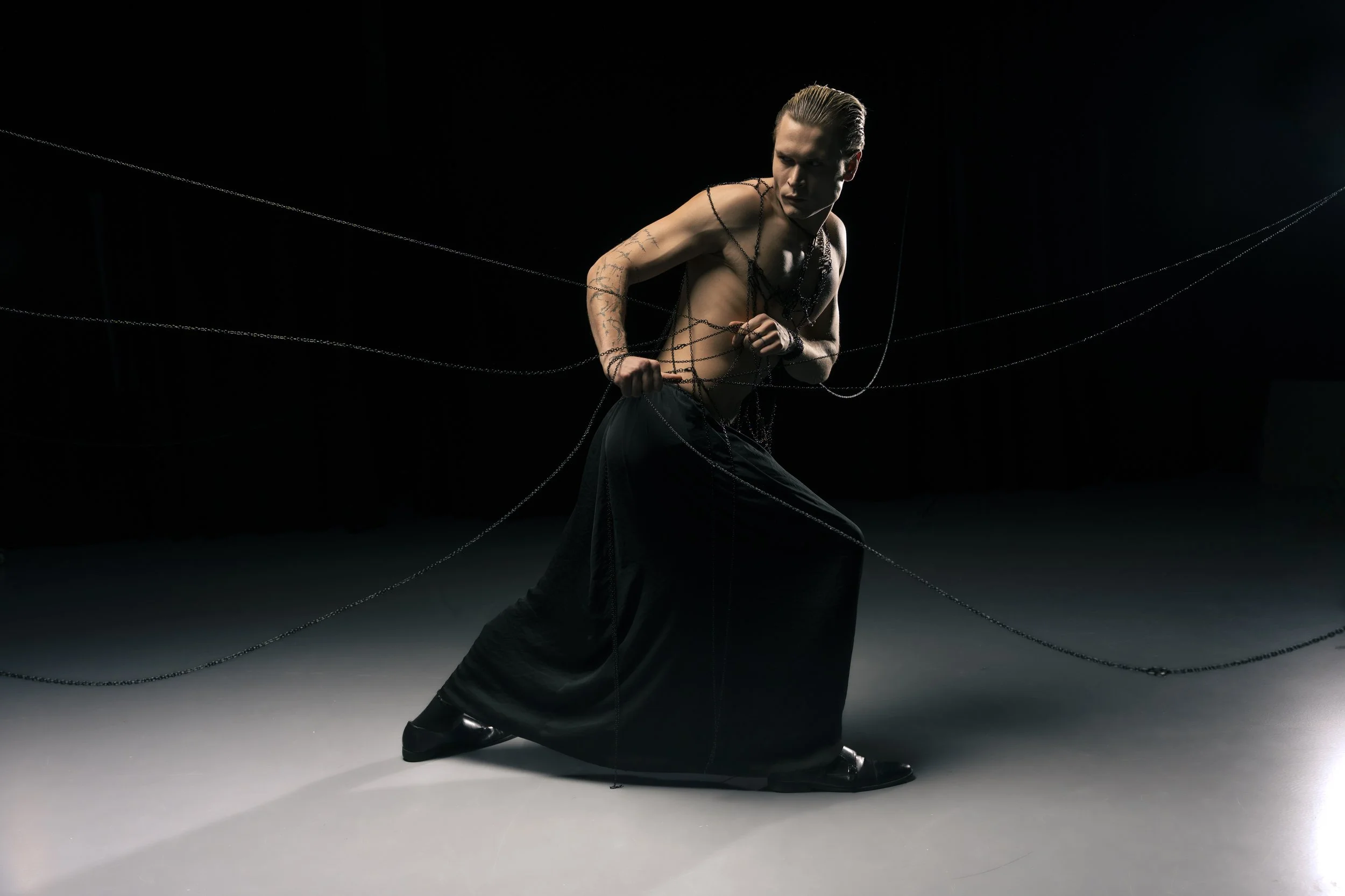 Mann in schwarzer Hose, keine Oberbekleidung, umgeben von dünnen schwarzen Linien, auf dunklem Hintergrund, in einer Pose mit geballten Fäusten.