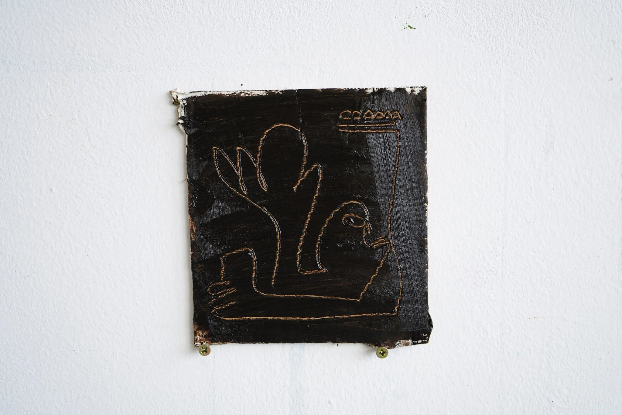 A small, rectangular, dark-colored painting with a metallic outline of a hand and a coffee cup, mounted on a white wall.
