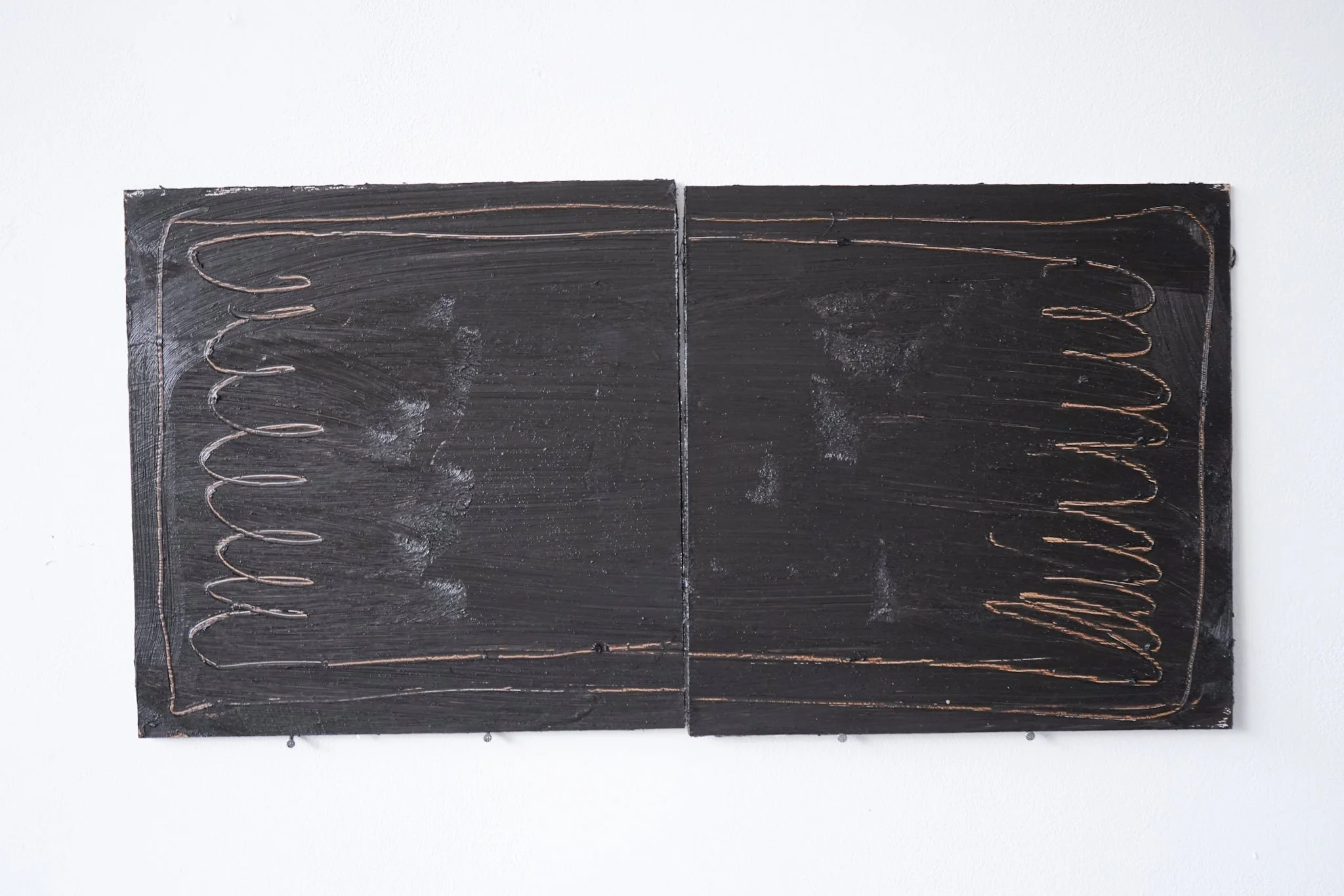 Two black rectangular panels mounted on a white wall, each with a copper wire spiral design.