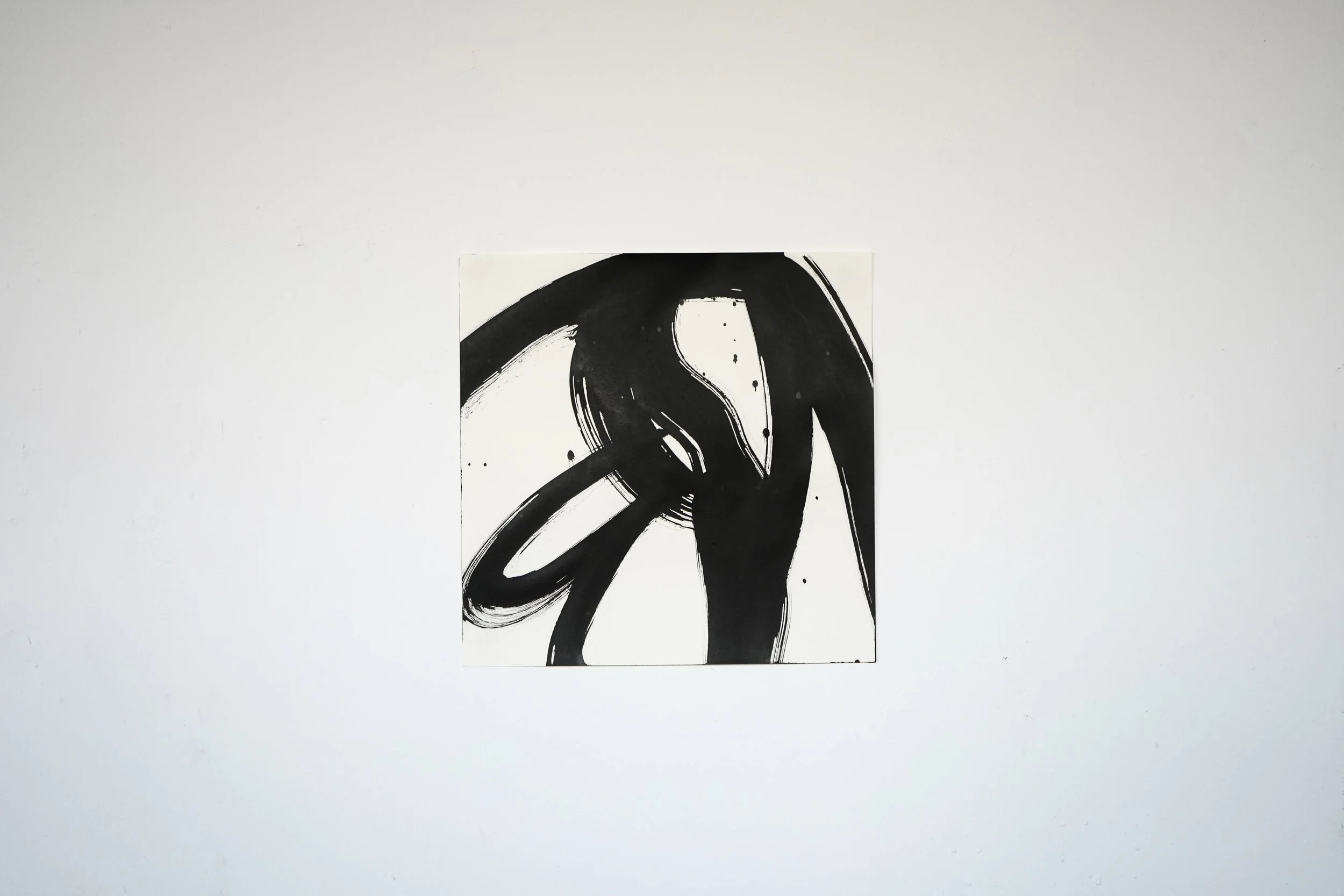 Black abstract ink brushstroke on white canvas hanging on a white wall.