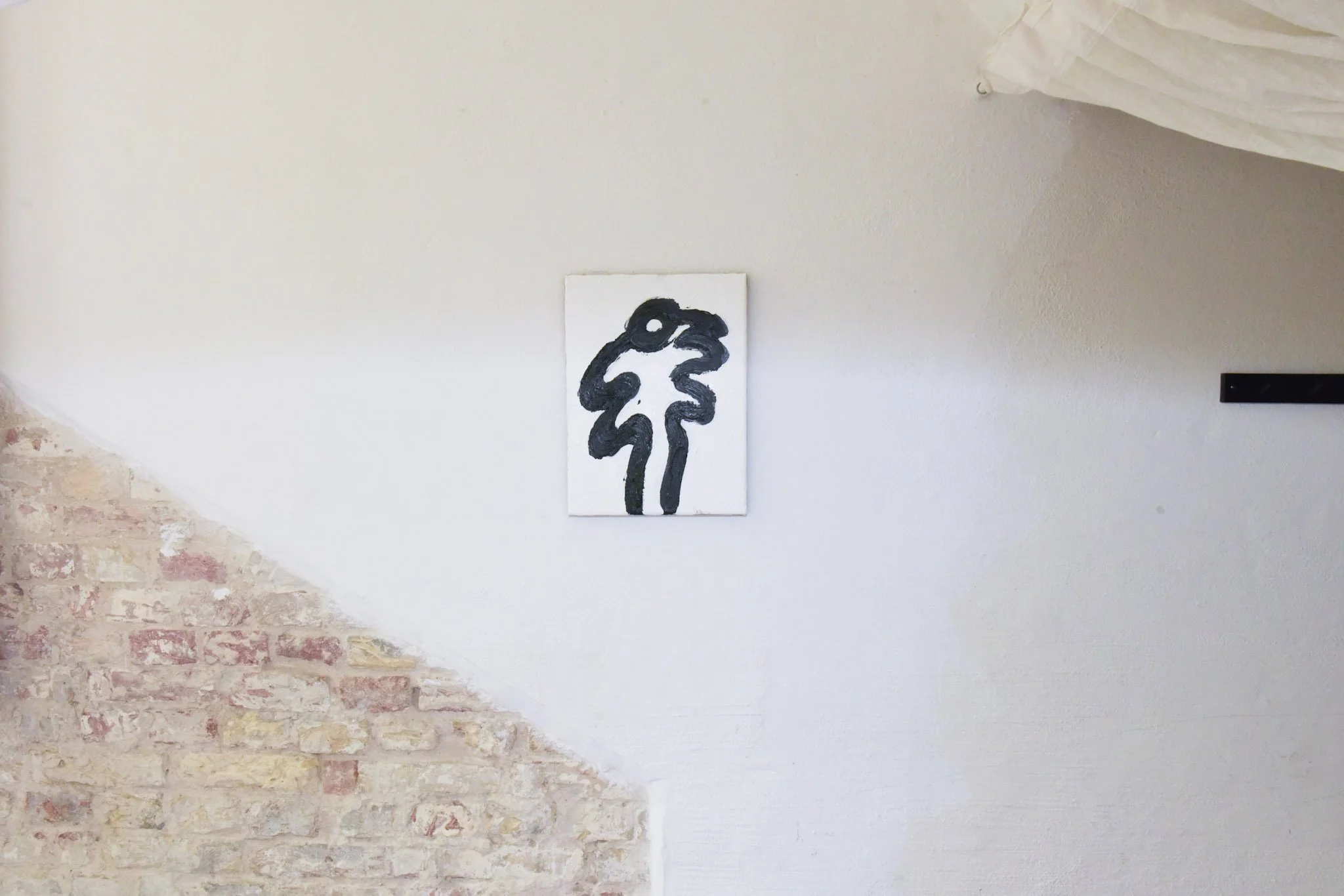 Contemporary abstract black and white painting of a stylized face on a white canvas, hung on a wall with exposed brick on the lower left.