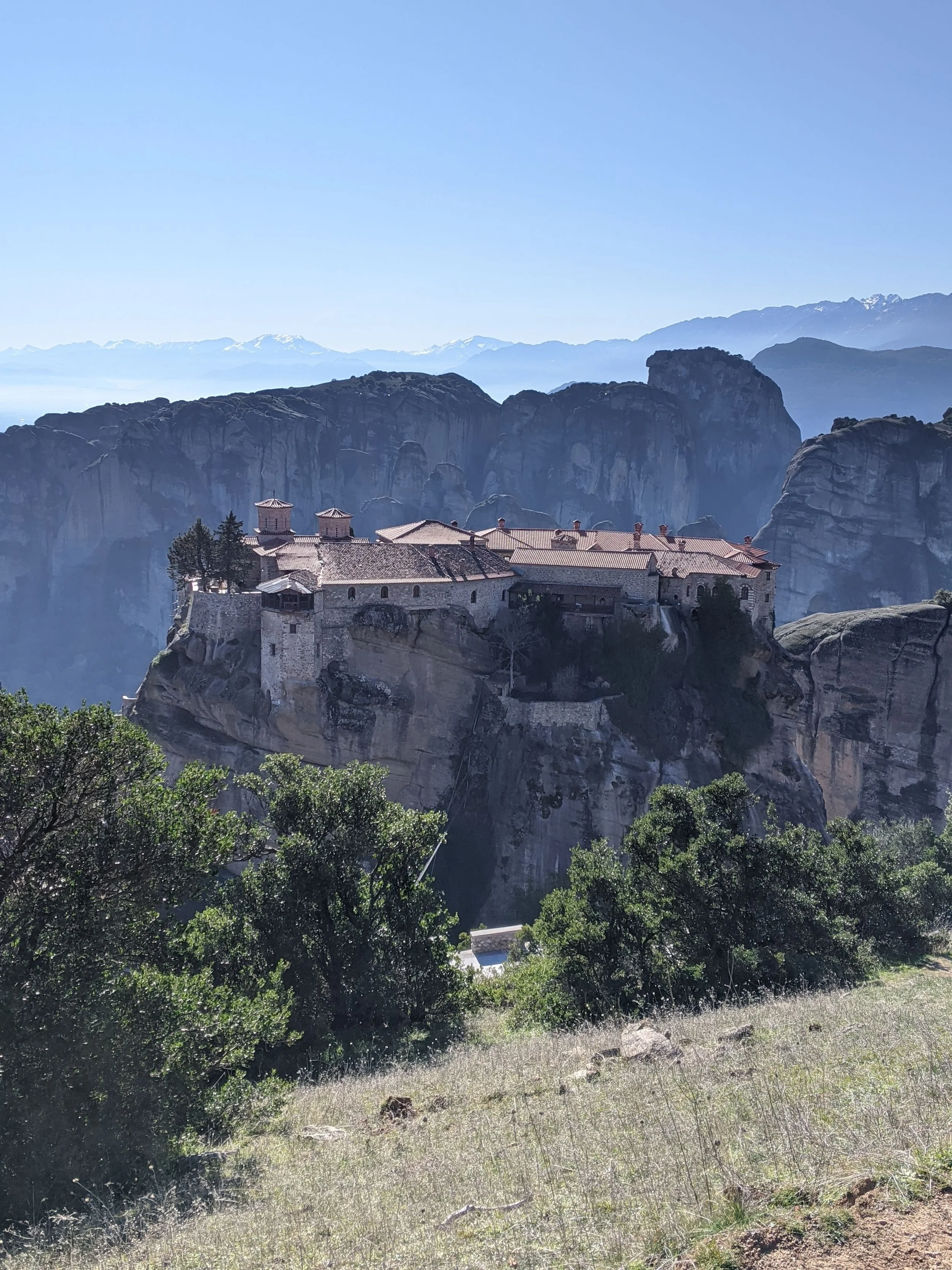 Cliffside monastery in Greece surrounded by trees and mountains—steeped in history and stillness