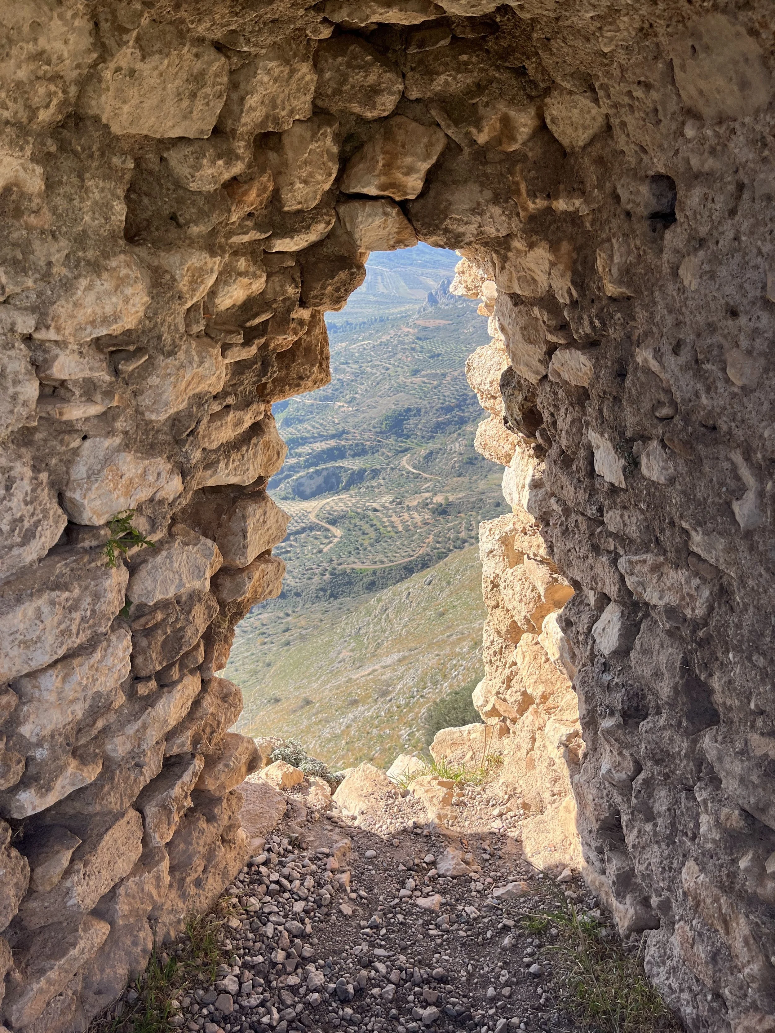Looking through a stone window onto terraced Tinos farmland—where nature, history, and tradition meet