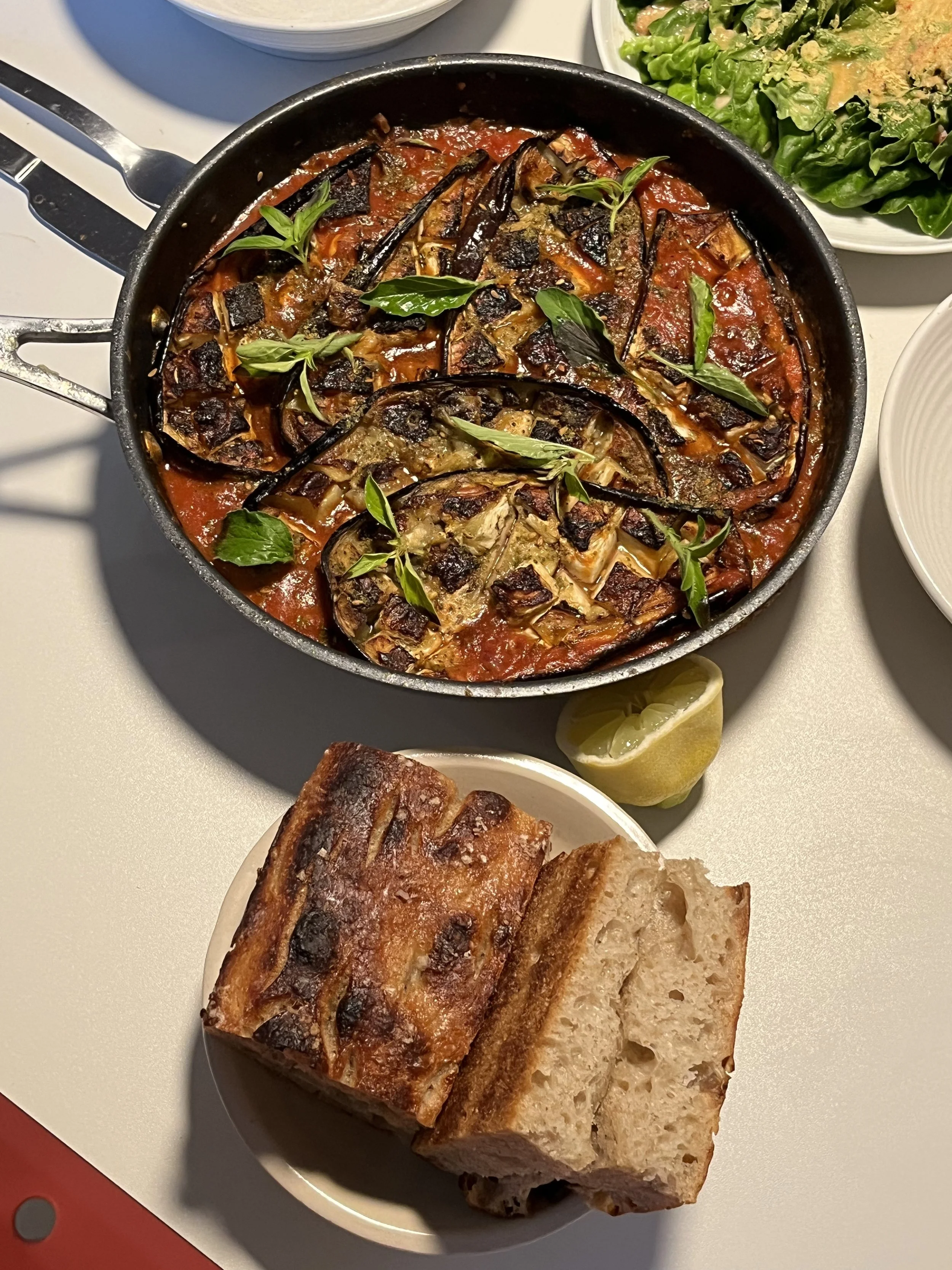 Roasted eggplant and tomato stew with fresh herbs, served with rustic bread and vibrant side salads at a Zengean retreat