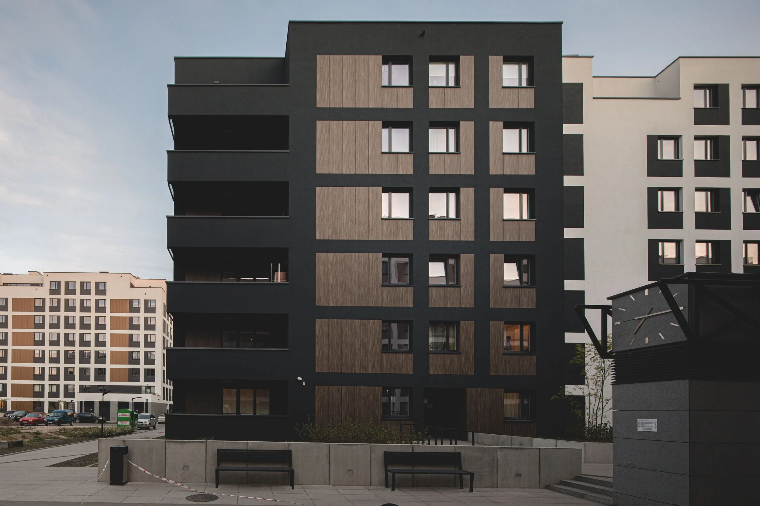 Modern multi-story apartment building with dark gray and wood exterior, balconies, and multiple windows.