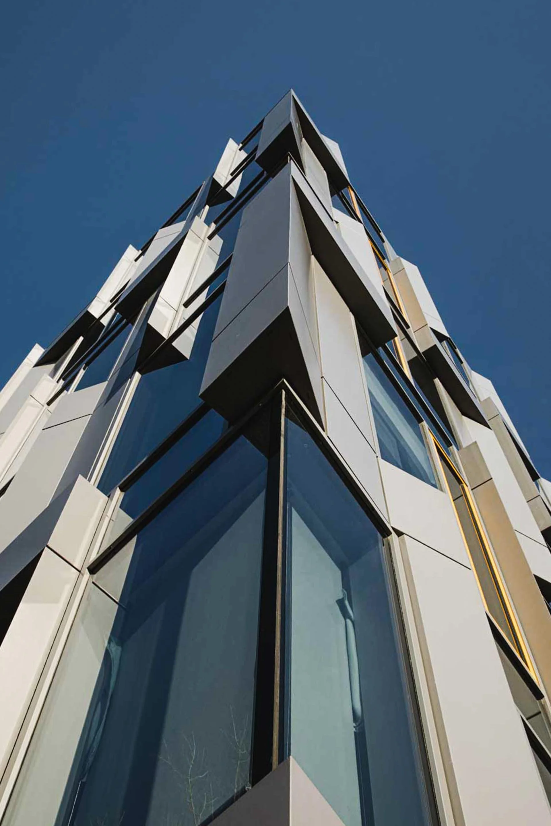 Low-angle view of a modern building with geometric shapes and glass windows against a clear blue sky.