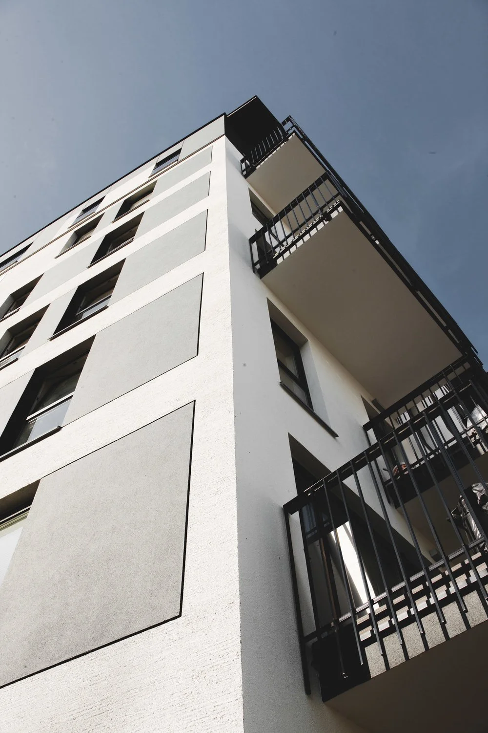 Close-up view of a modern white apartment building with black railings and balconies against a clear blue sky.
