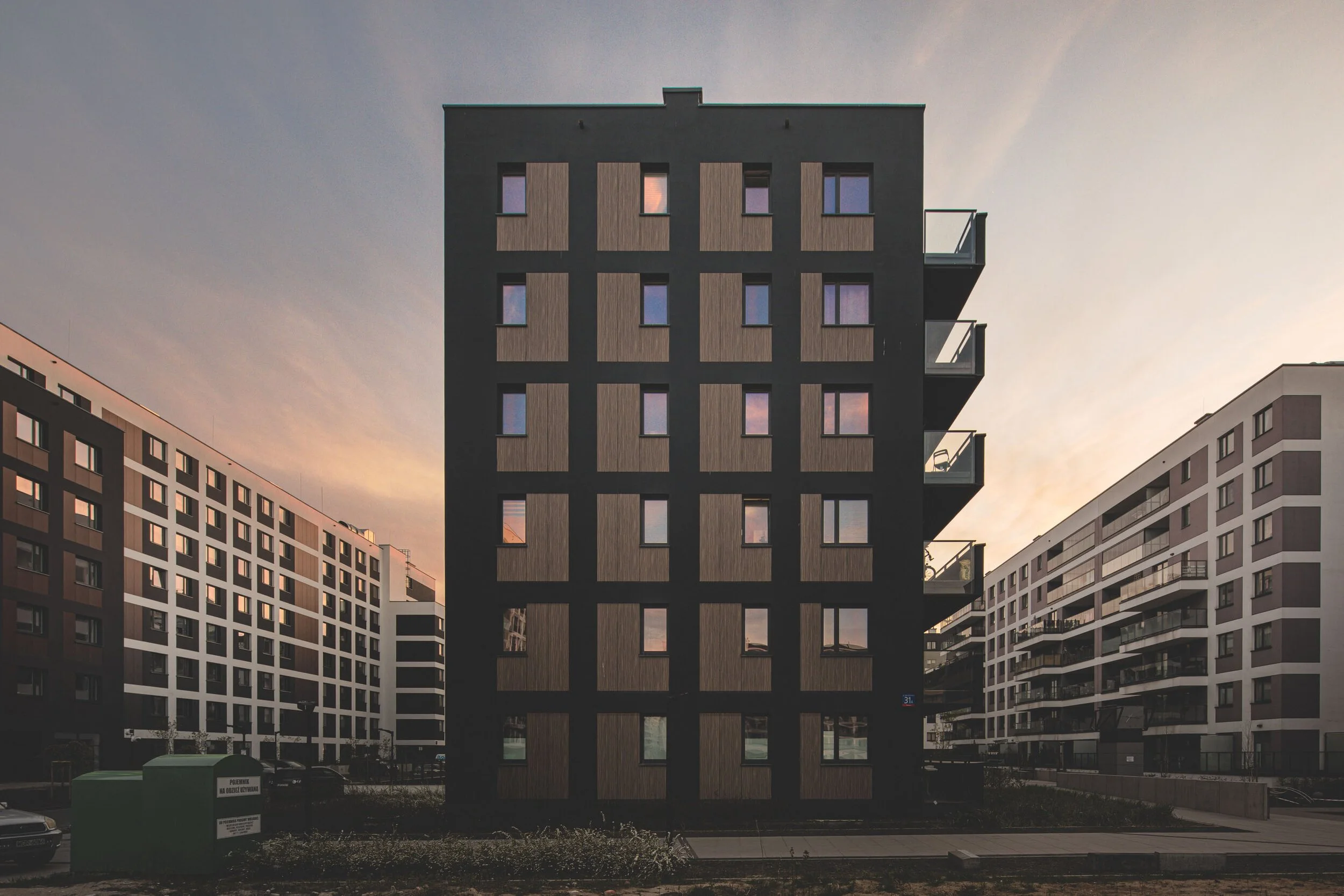 Modern black apartment building with multiple small windows and balconies, in an urban setting during sunset