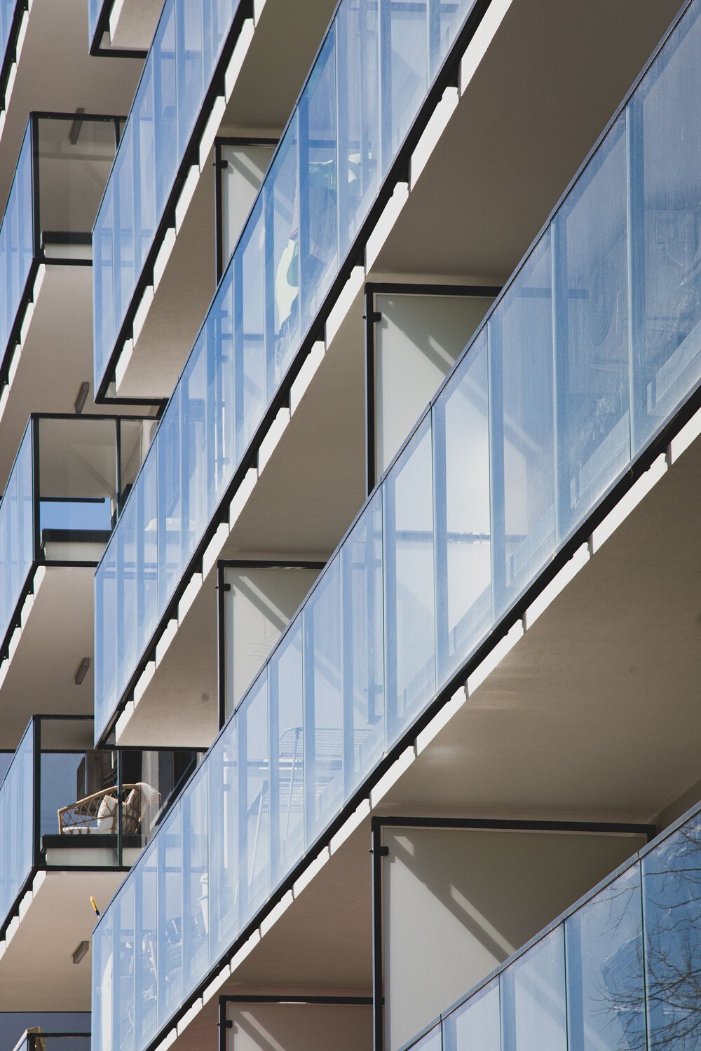 Multiple apartment balconies with glass railings on a modern building.