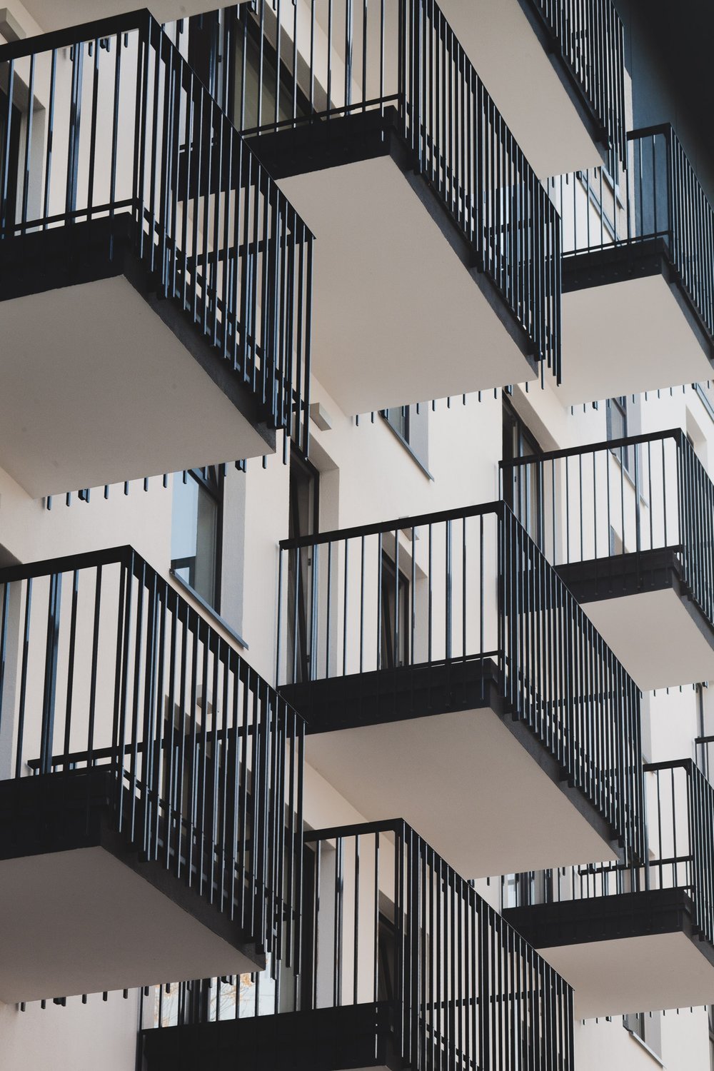 Multiple building balconies with black metal railings and white concrete floors.